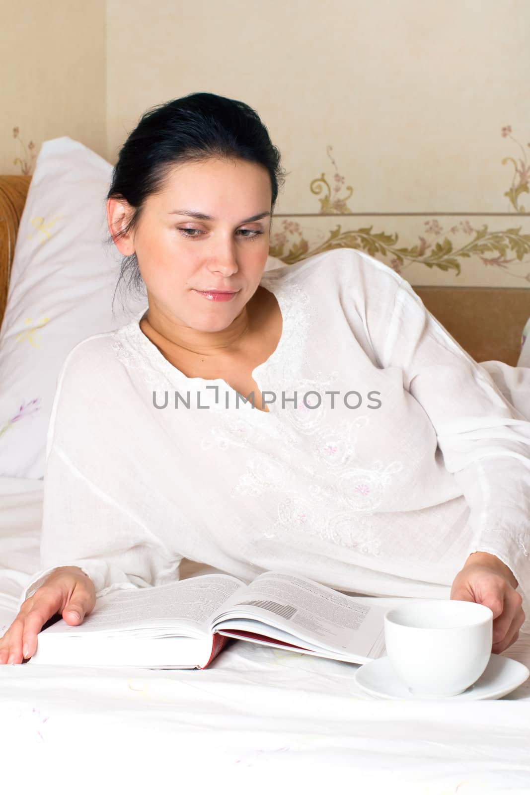 Portrait of young woman with white cup and book on bed at bedroom