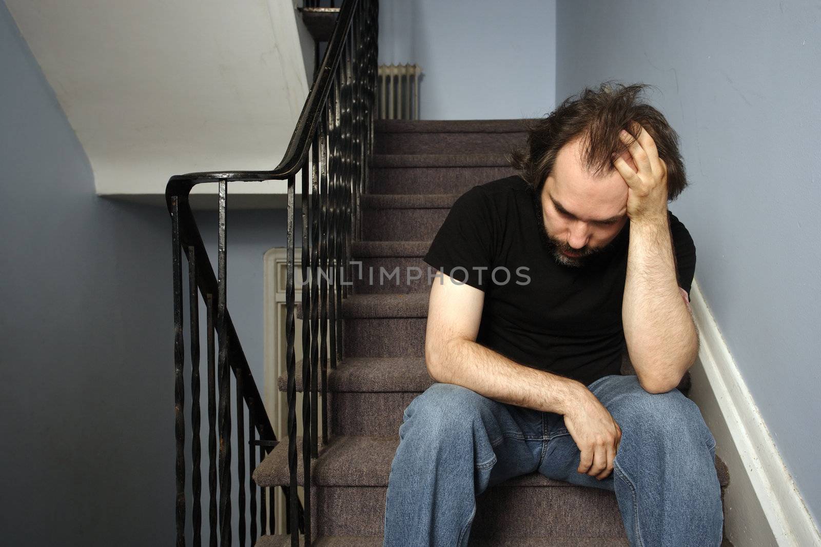 A male adult with serious depression sitting in the stairwell of his apartment building.
