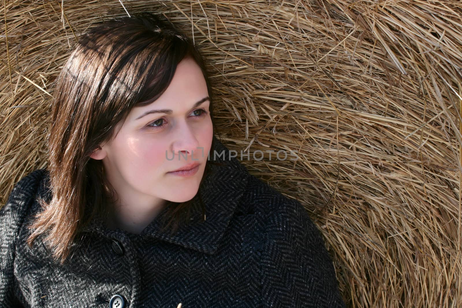 Beautiful brunette female sitting against a hay bale