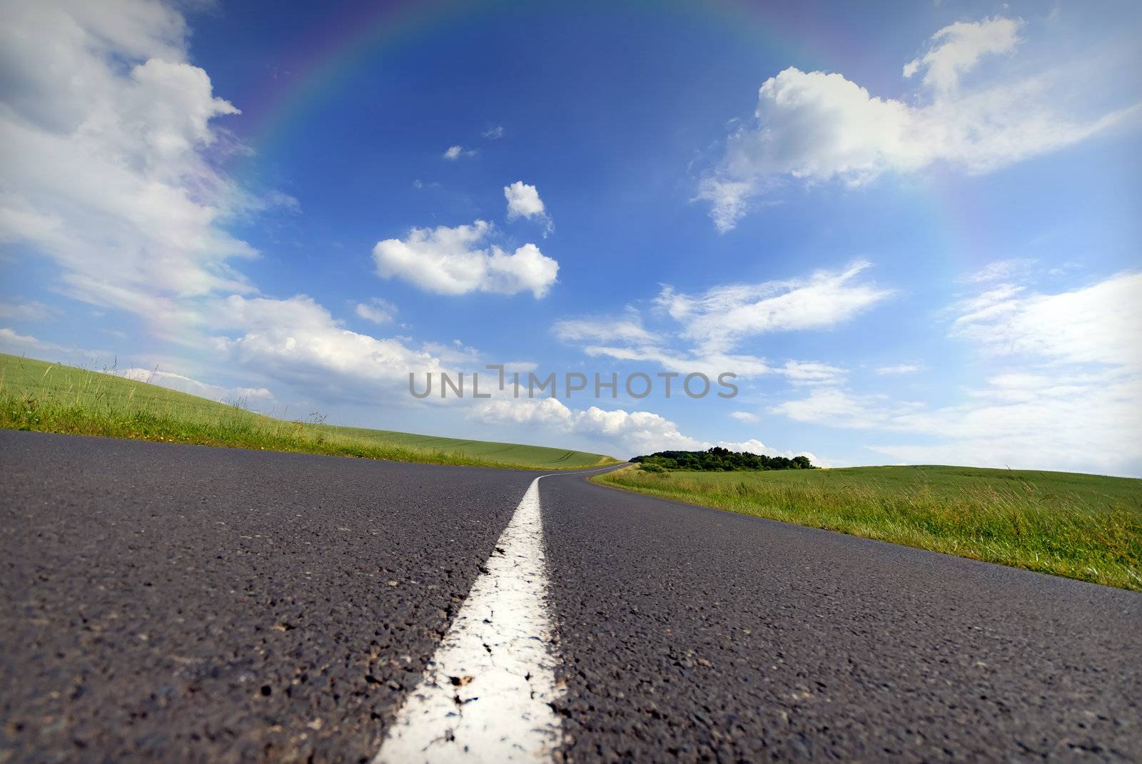 An empty road with a white line down the middle and surrounded by a rainbow