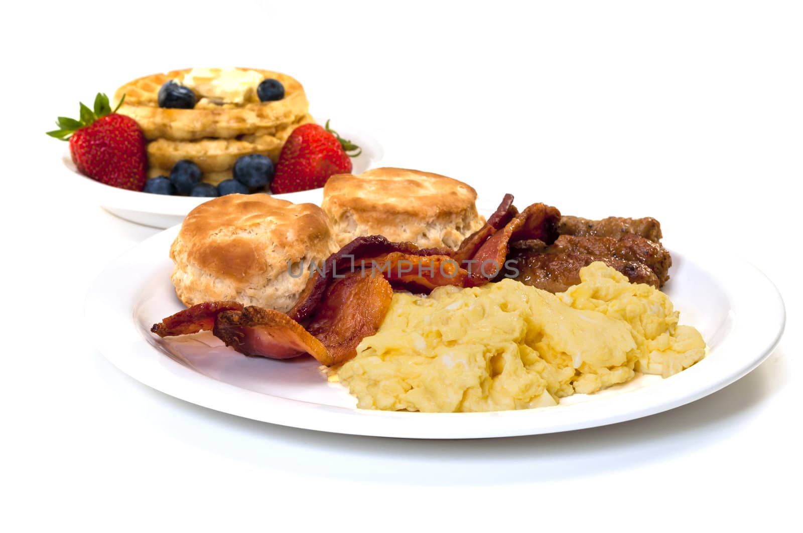 Scrambled eggs, bacon, link sausage, biscuits,  and waffles with strawberries and blueberries.  Isolated on white background.