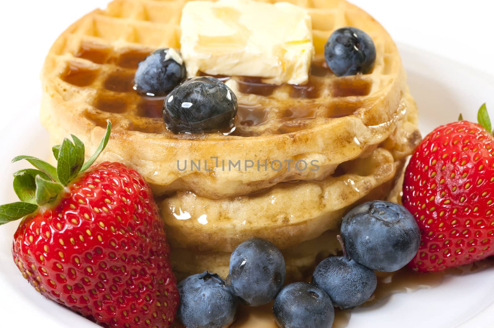 Closeup of waffles, strawberries, blueberries, and butter.   Isolated on white background.