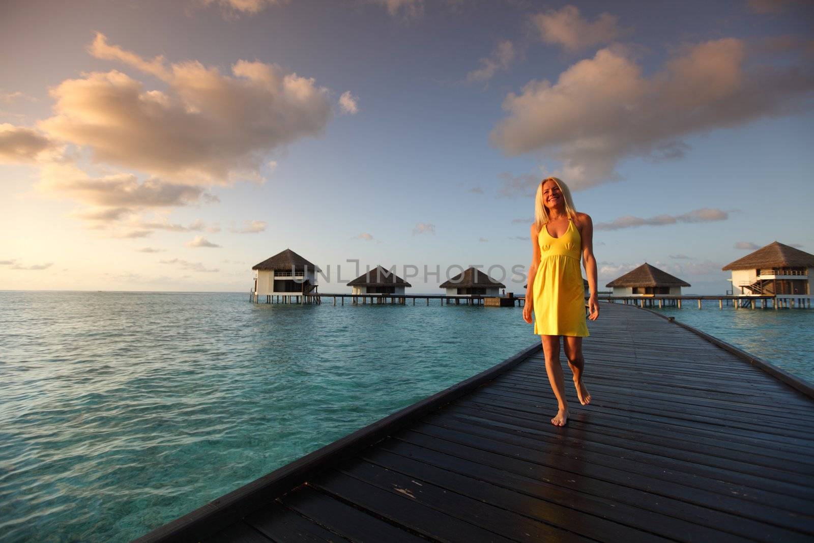 woman in a dress on a bridge home sea and the maldivian sunset on the background