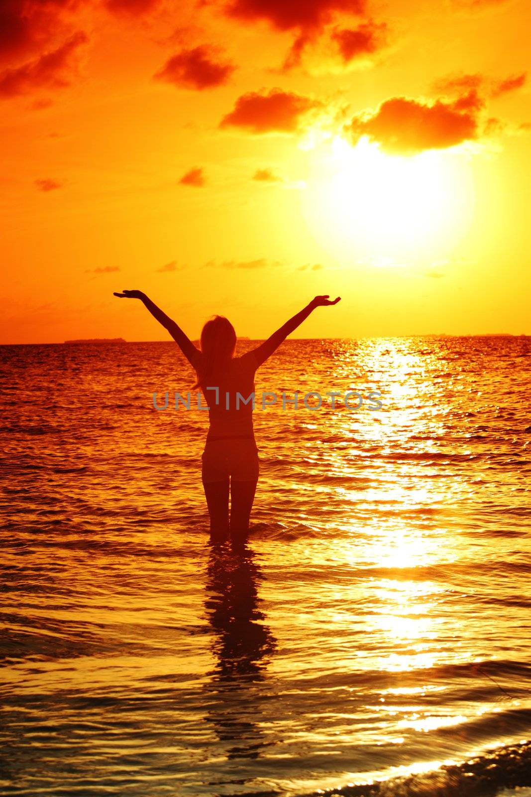 happy woman standing on a sunset in ocean waves