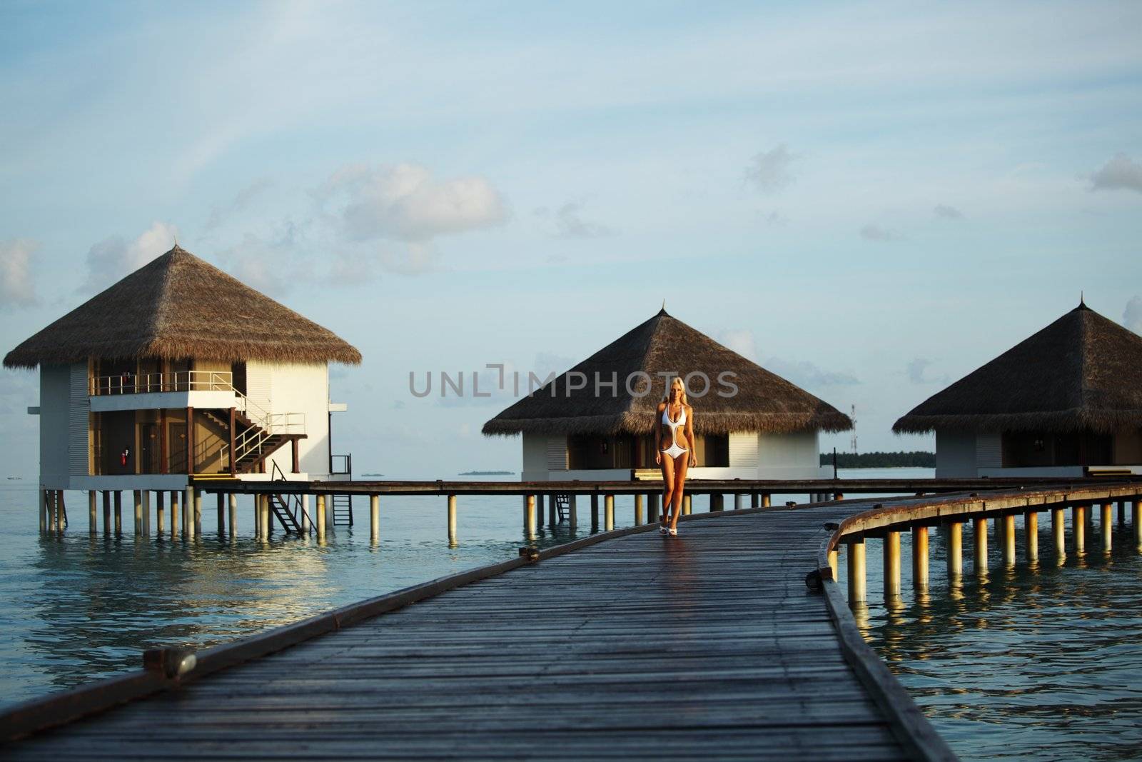 woman in a dress on a bridge home sea and the maldivian sunset on the background