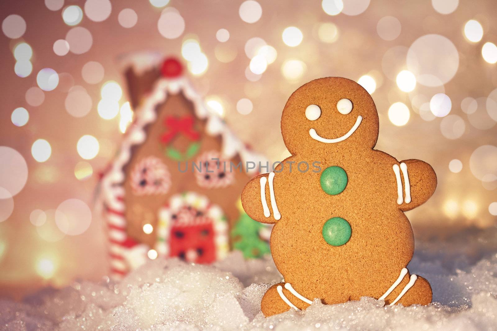 Gingerbread man cookie standing in snow beside house 