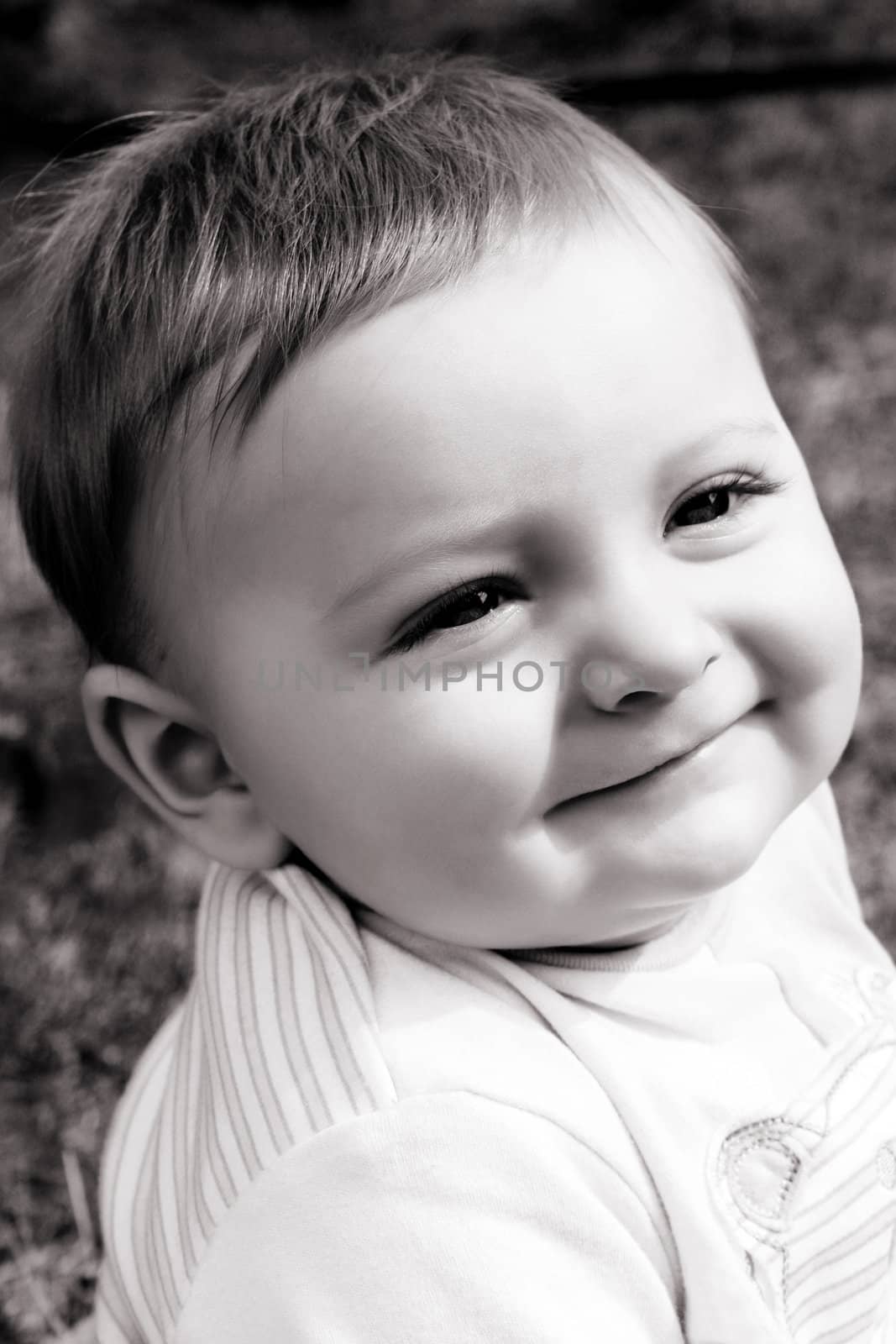 Adorable baby boy sitting outside in the sunny garden 