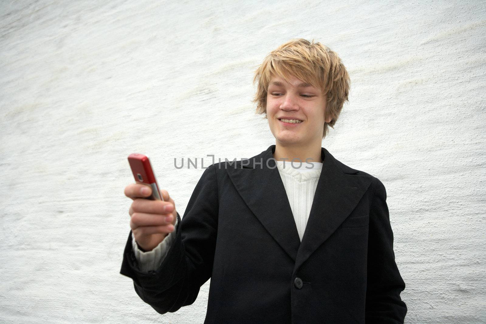 Smiling teenage boy looking at mobile phone by building wall