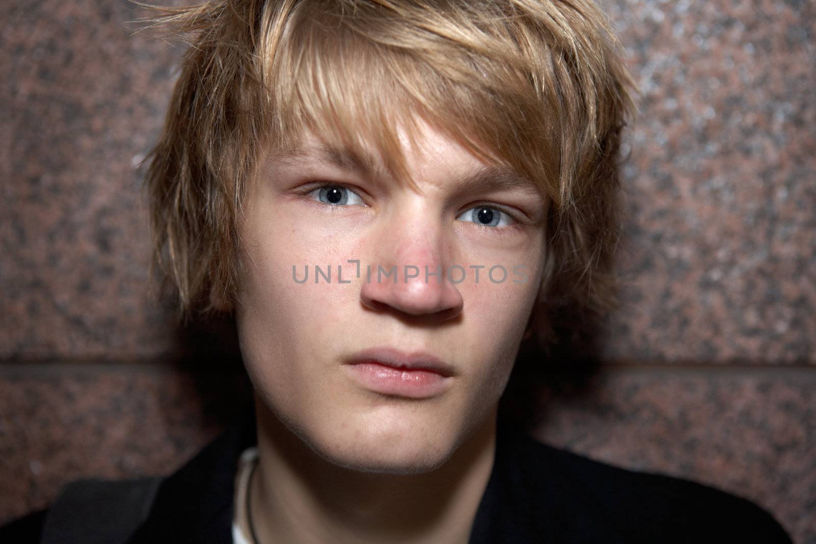 Close-up of teenage boy leaning against outside wall, looking at camera