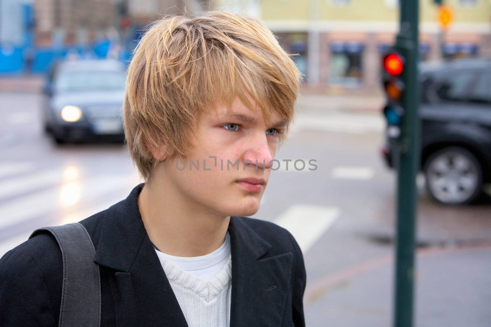 Teenage boy in street, looking away, traffic in background