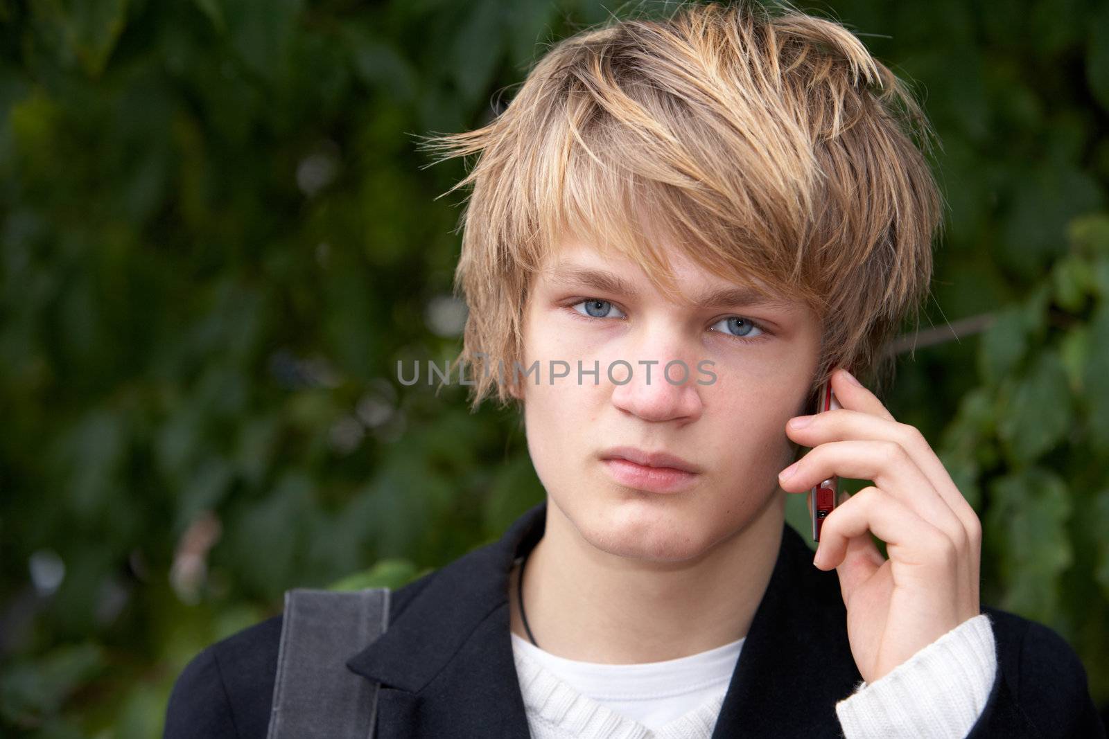 Teenage boy using mobile phone in city park, looking at camera