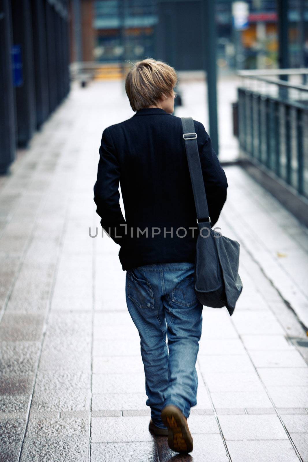 Teenage boy walking away from camera in street, motion blur