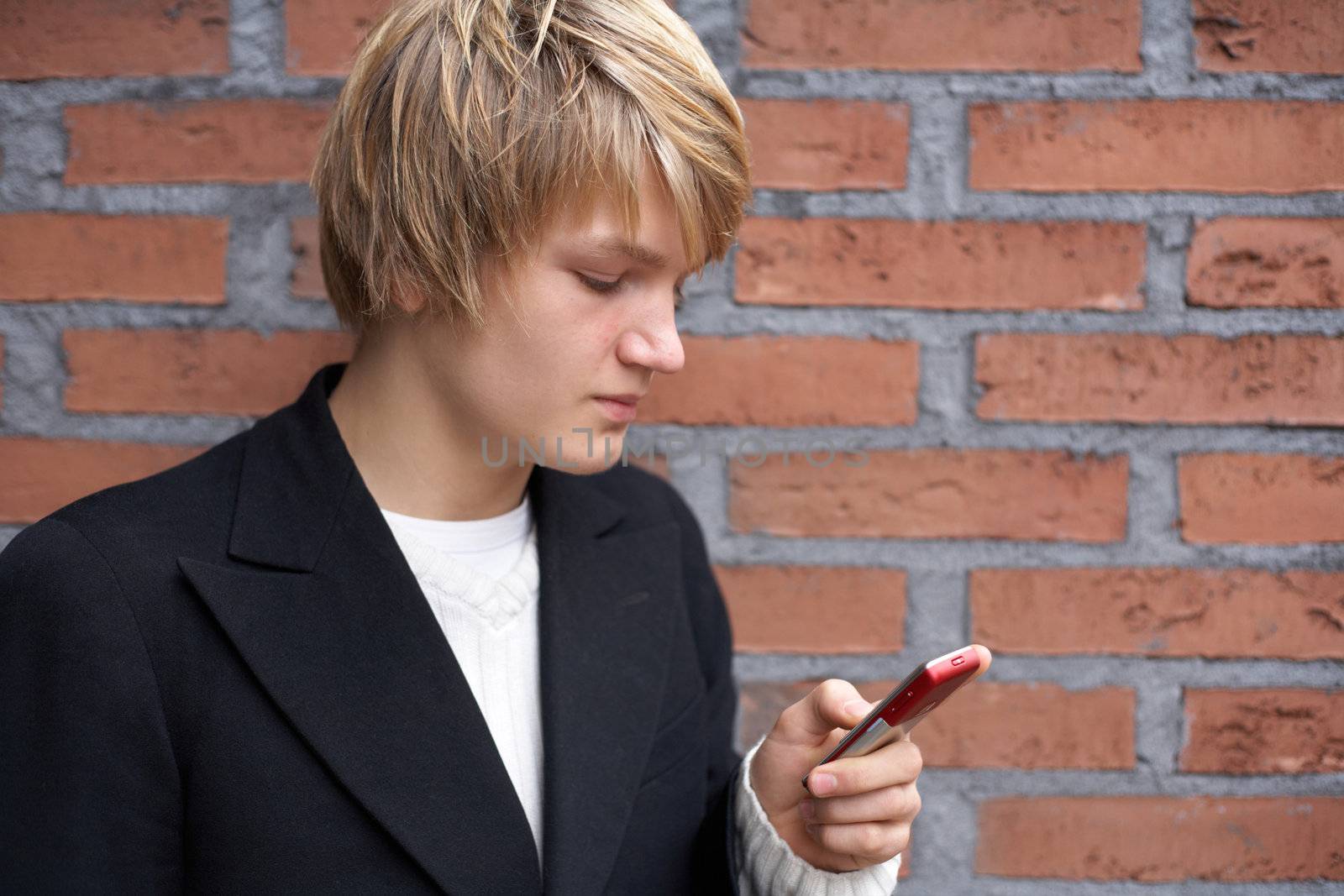 Teenage boy text messaging with mobile phone by brick wall