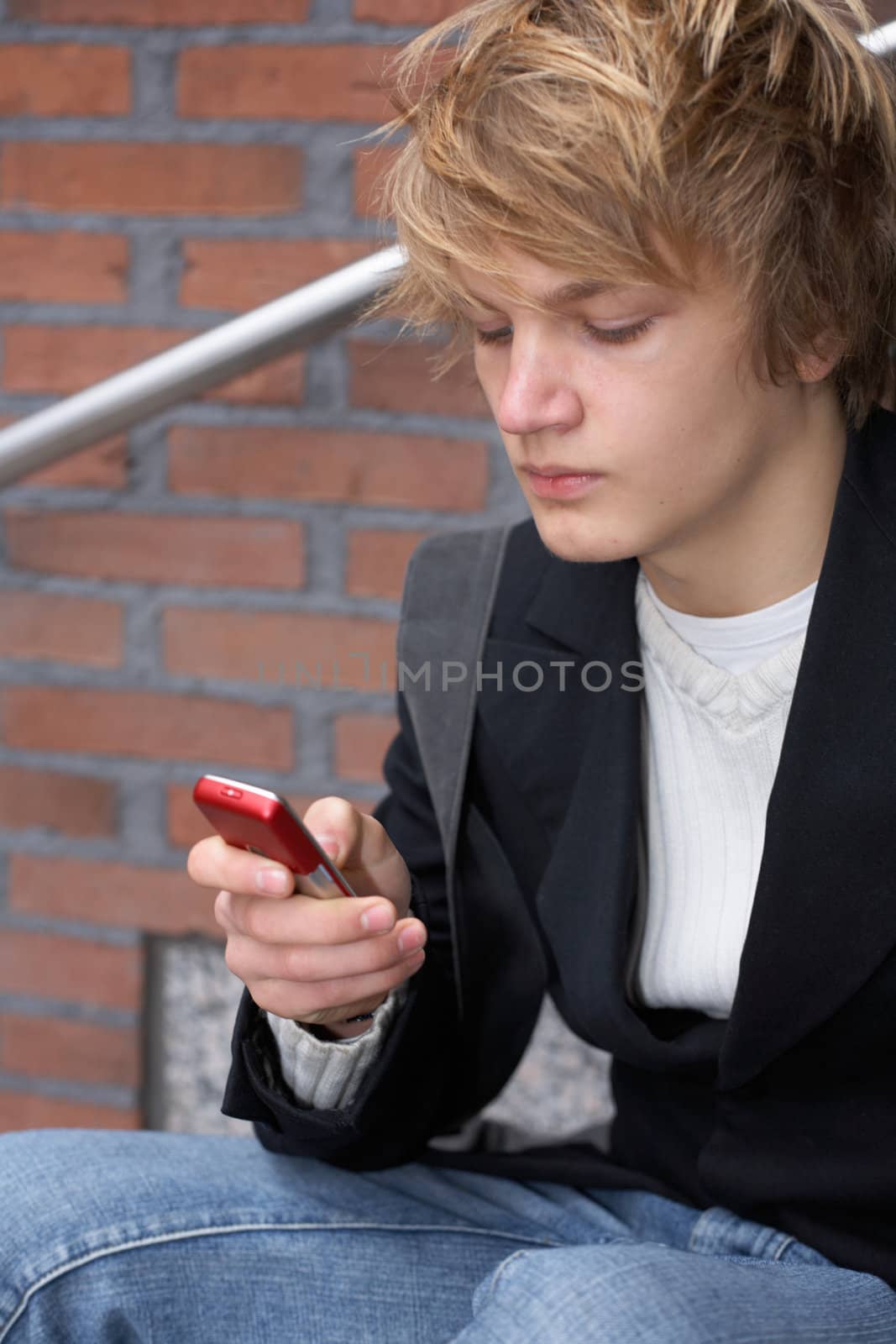 Teenage boy text messaging with mobile phone by building