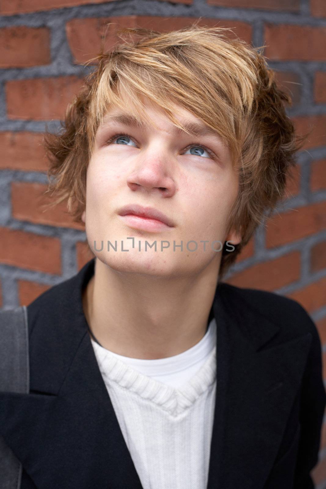 Teenage boy looking up to sky near brick wall