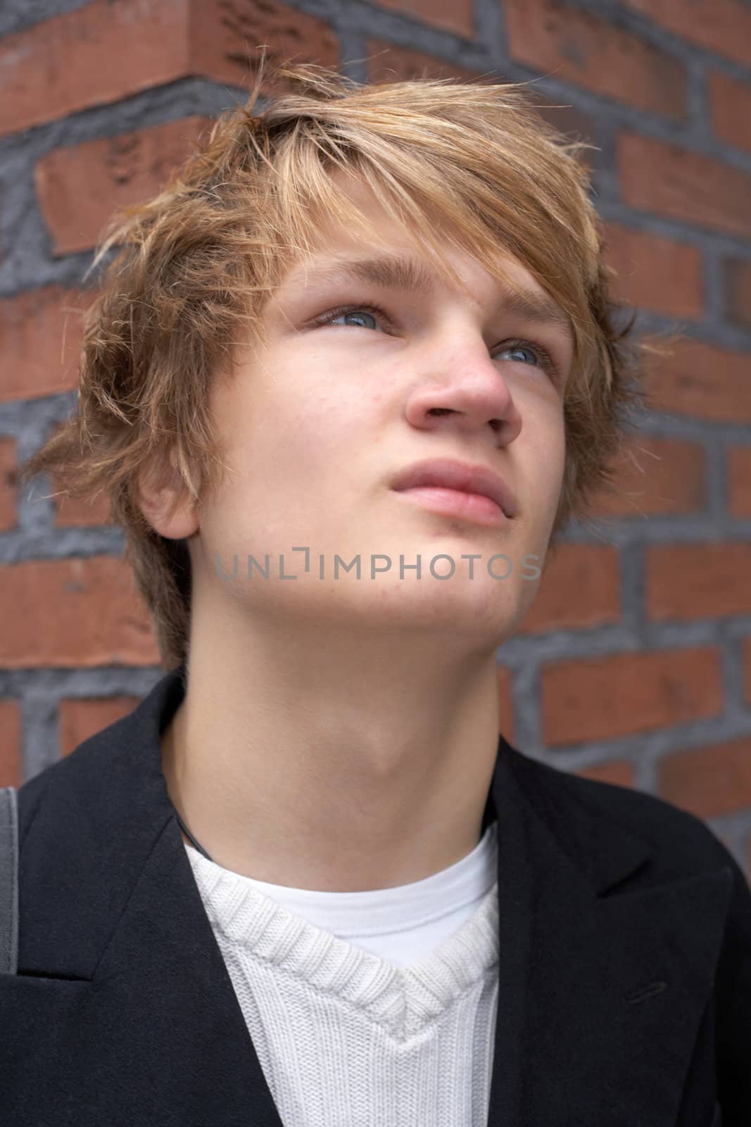 Pensive teenage boy by brick wall, looking away