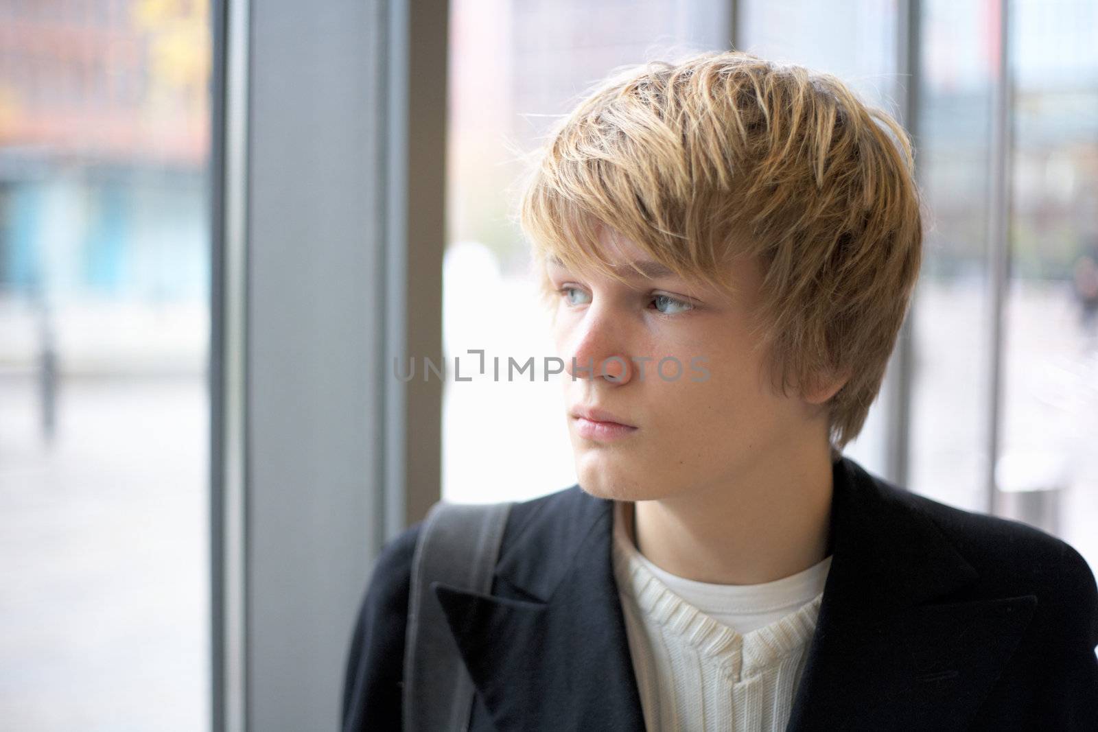 Teenage boy looking out window in urban environment, interior