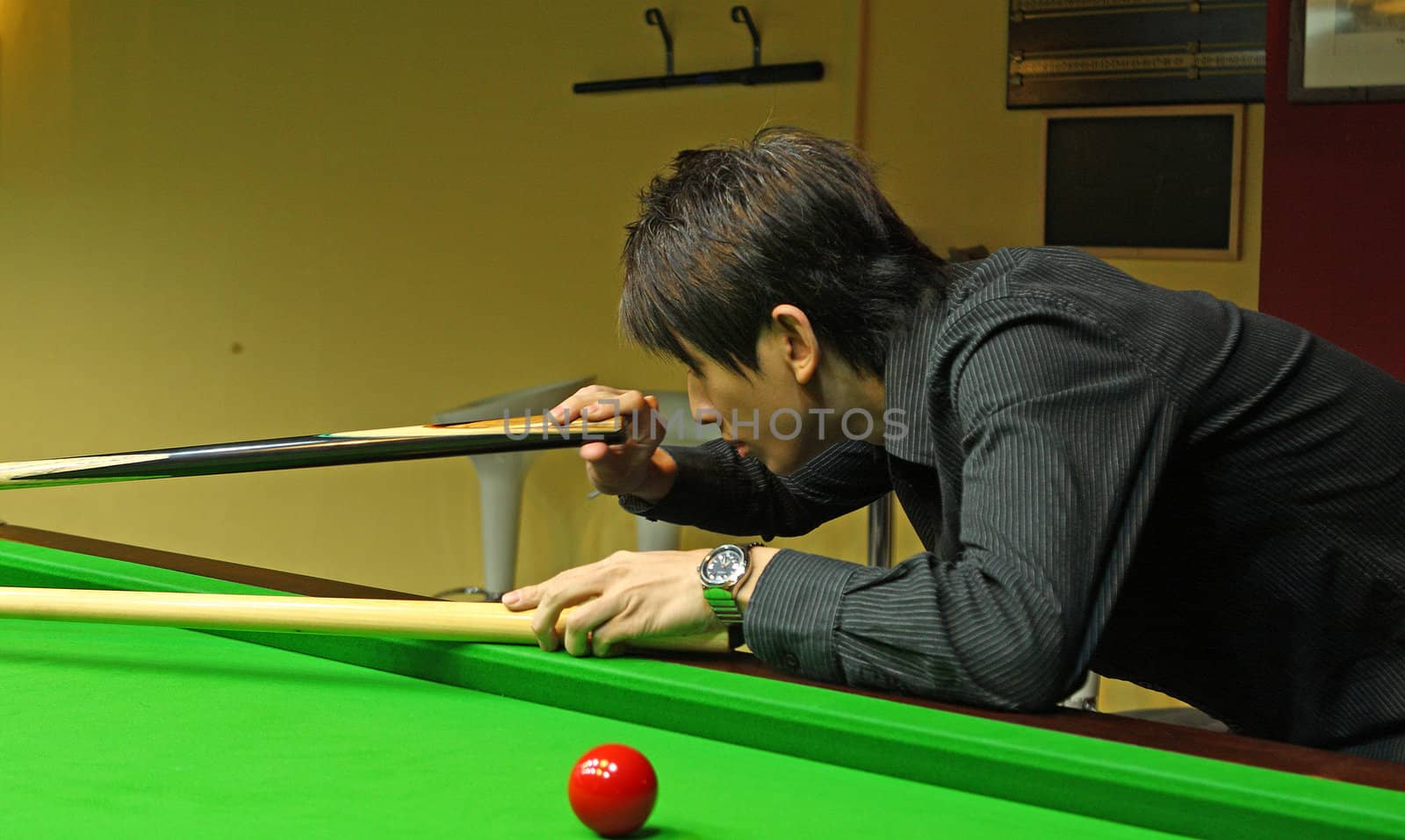 Young man concentrating while aiming at pool ball while playing billiards. 