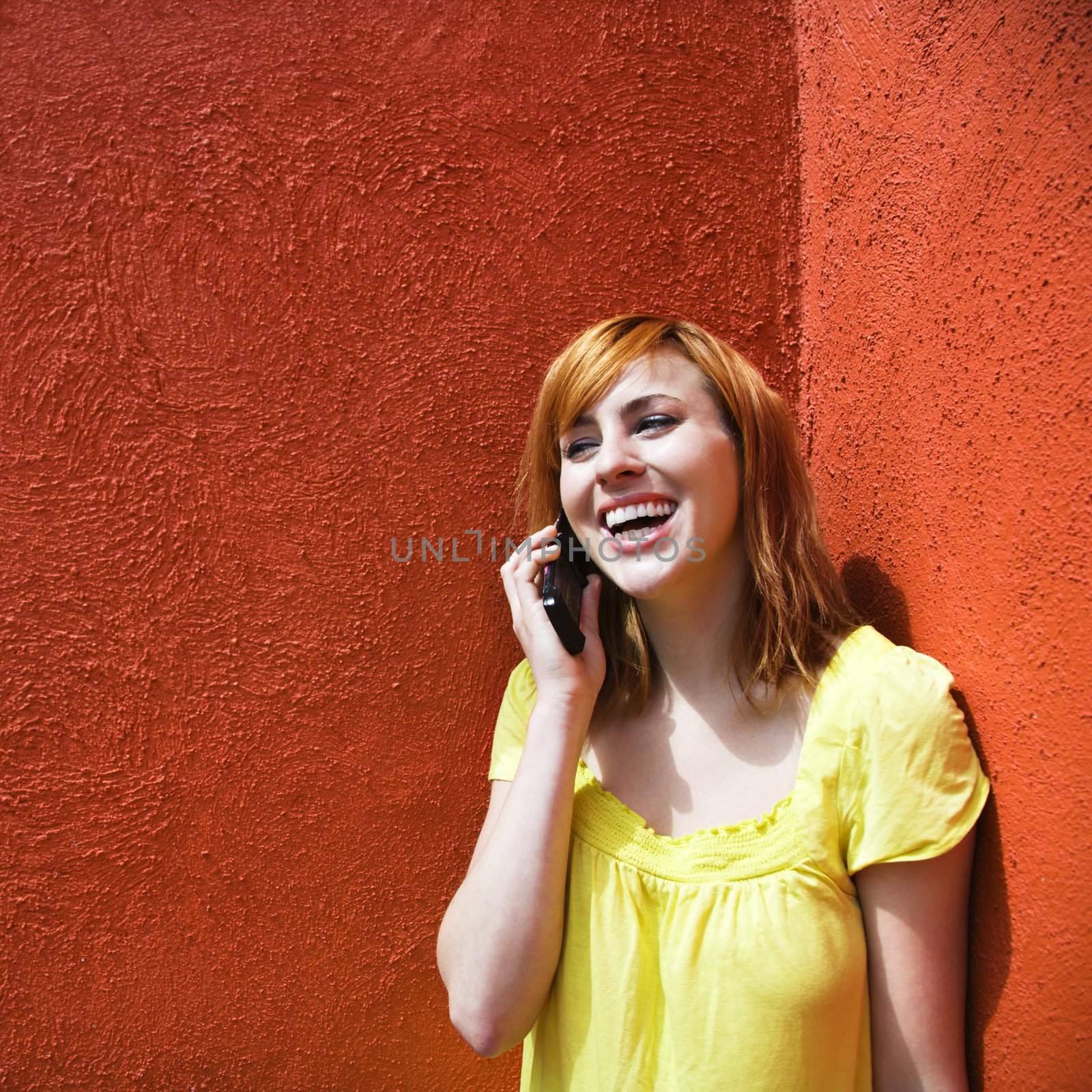 Smiling young redhead female talking on cellphone.