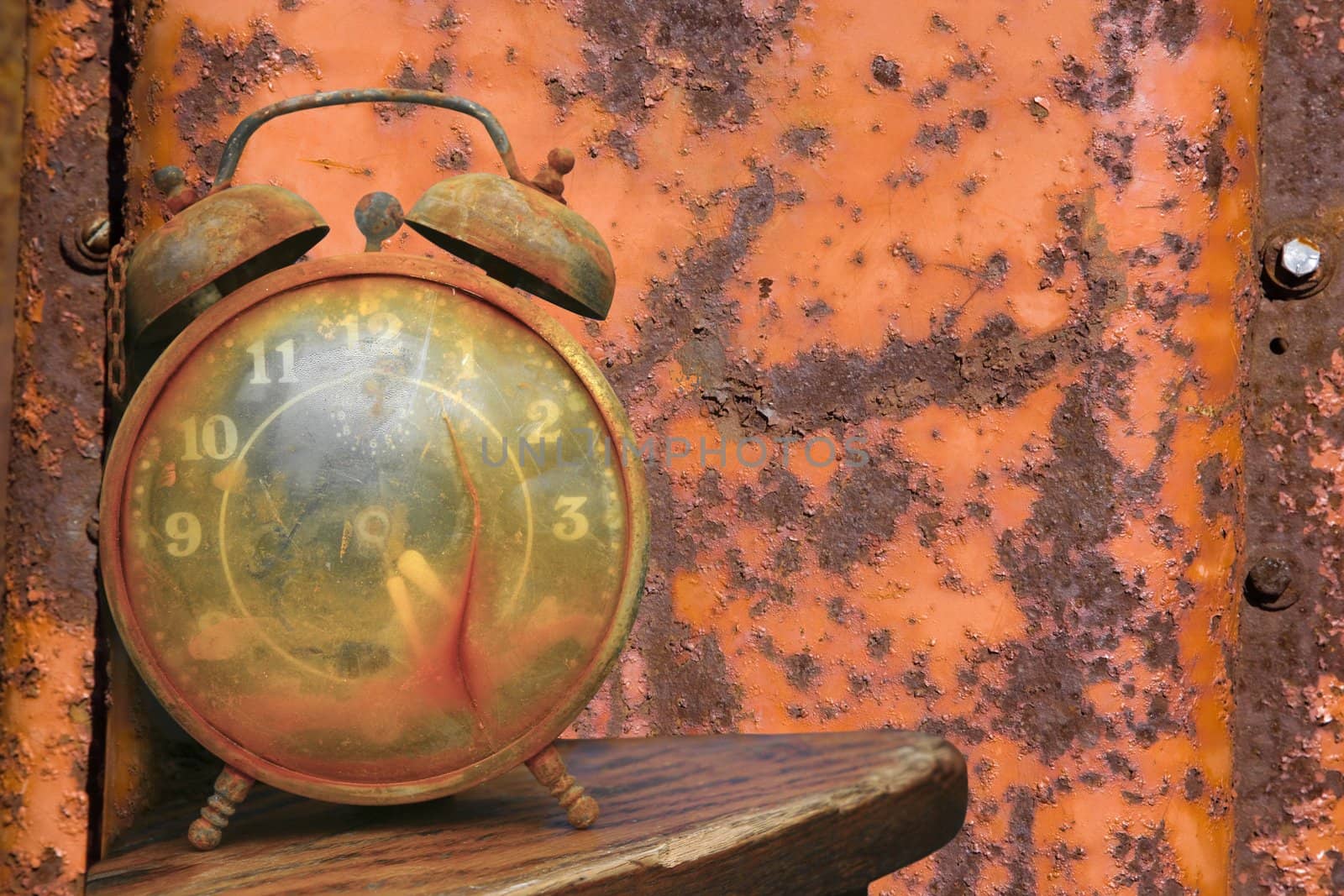 Old weathered alarm clock against rusty orange metal background.
