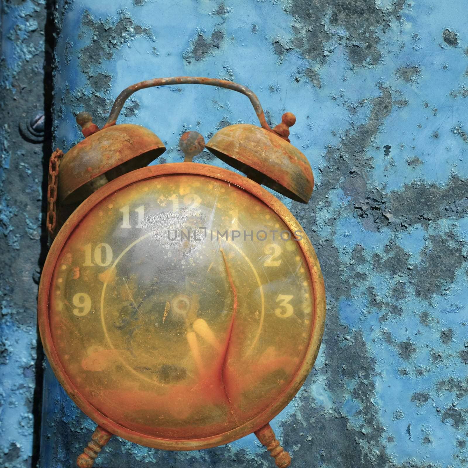 Old weathered alarm clock against rusty blue metal background.