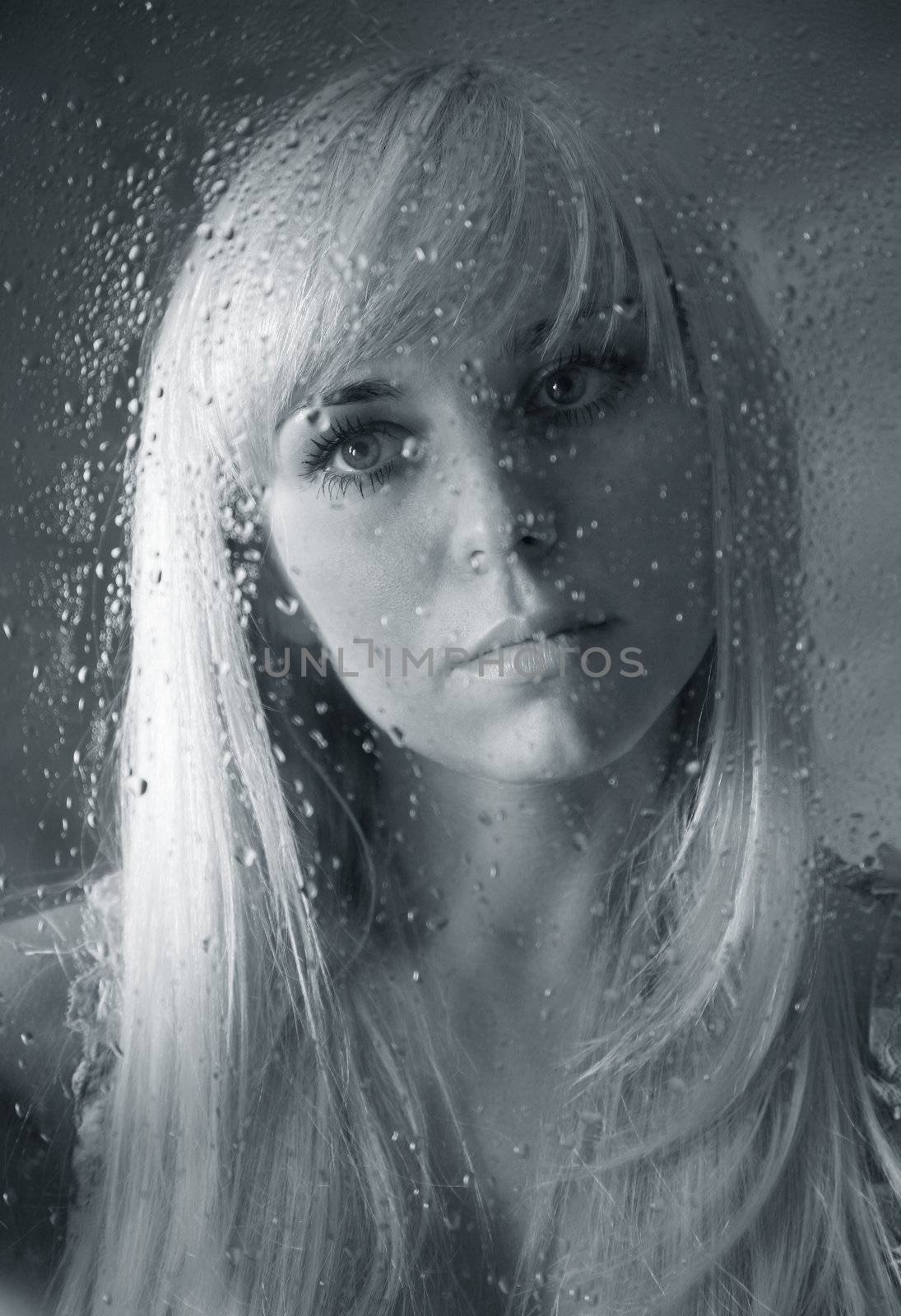 The beautiful girl behind wet glass