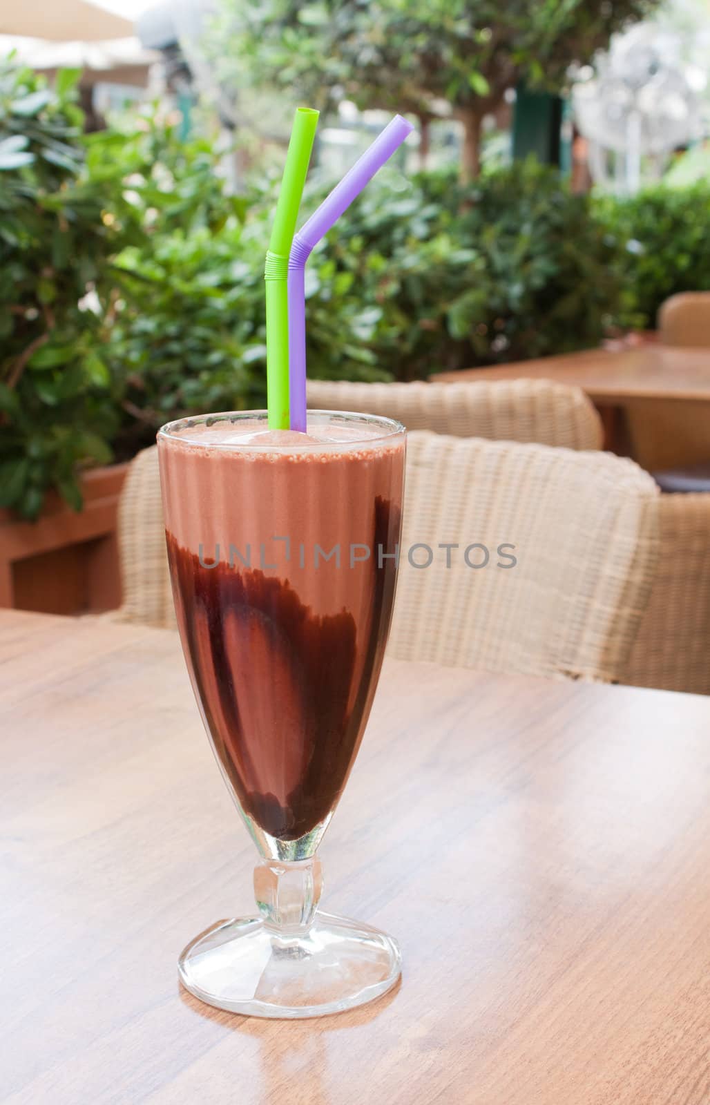 A chocolate milkshake on an outside table of a cafeteria.