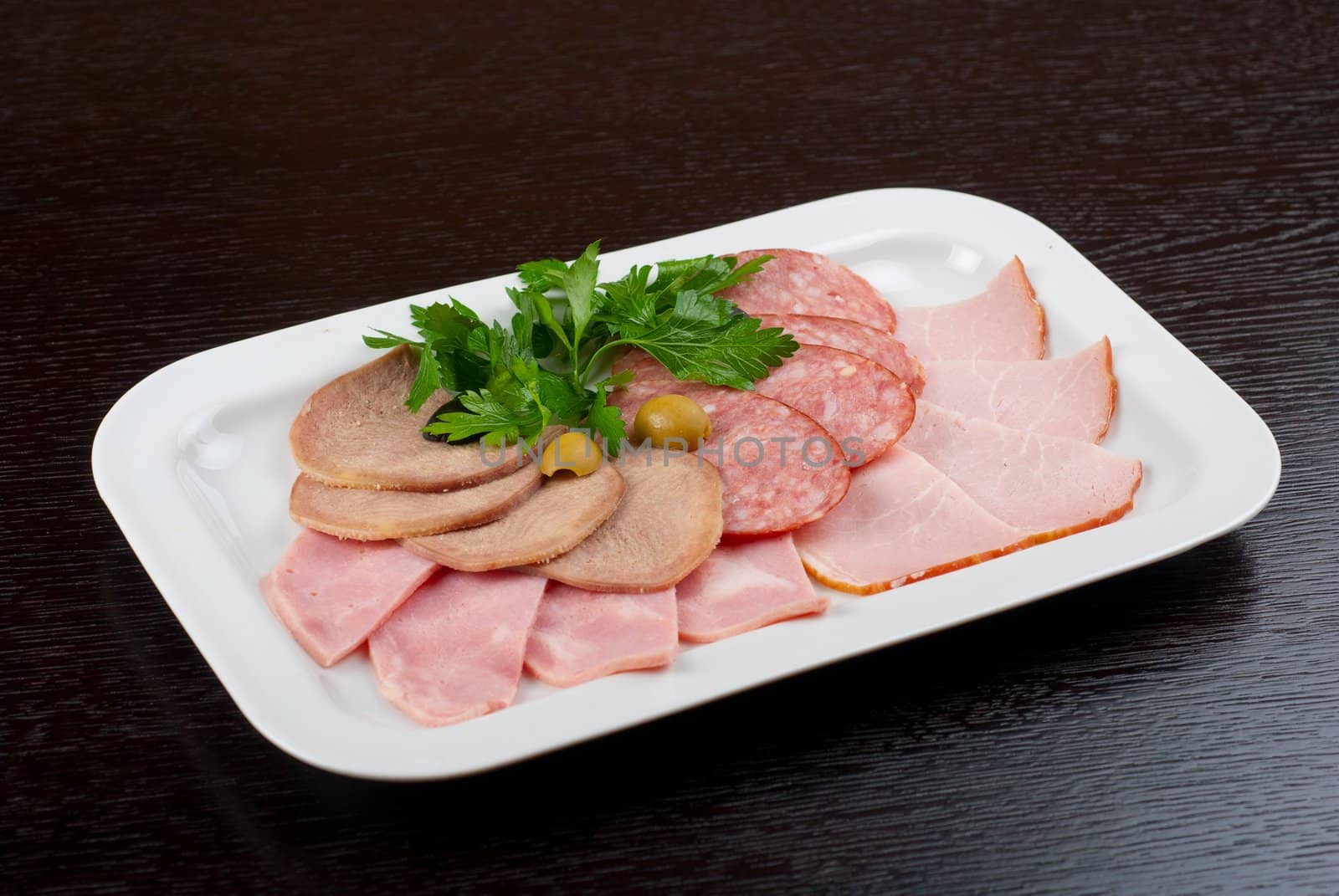 Meat assortment of beef tongue, sausage, meat and ham with greens