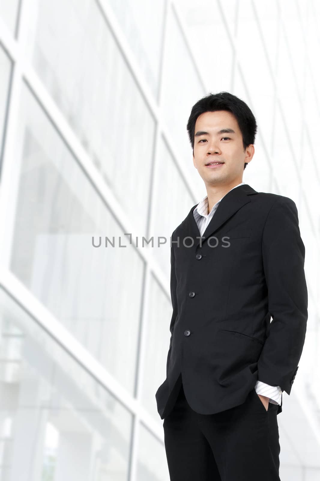 Young Asian executive standing against office building background