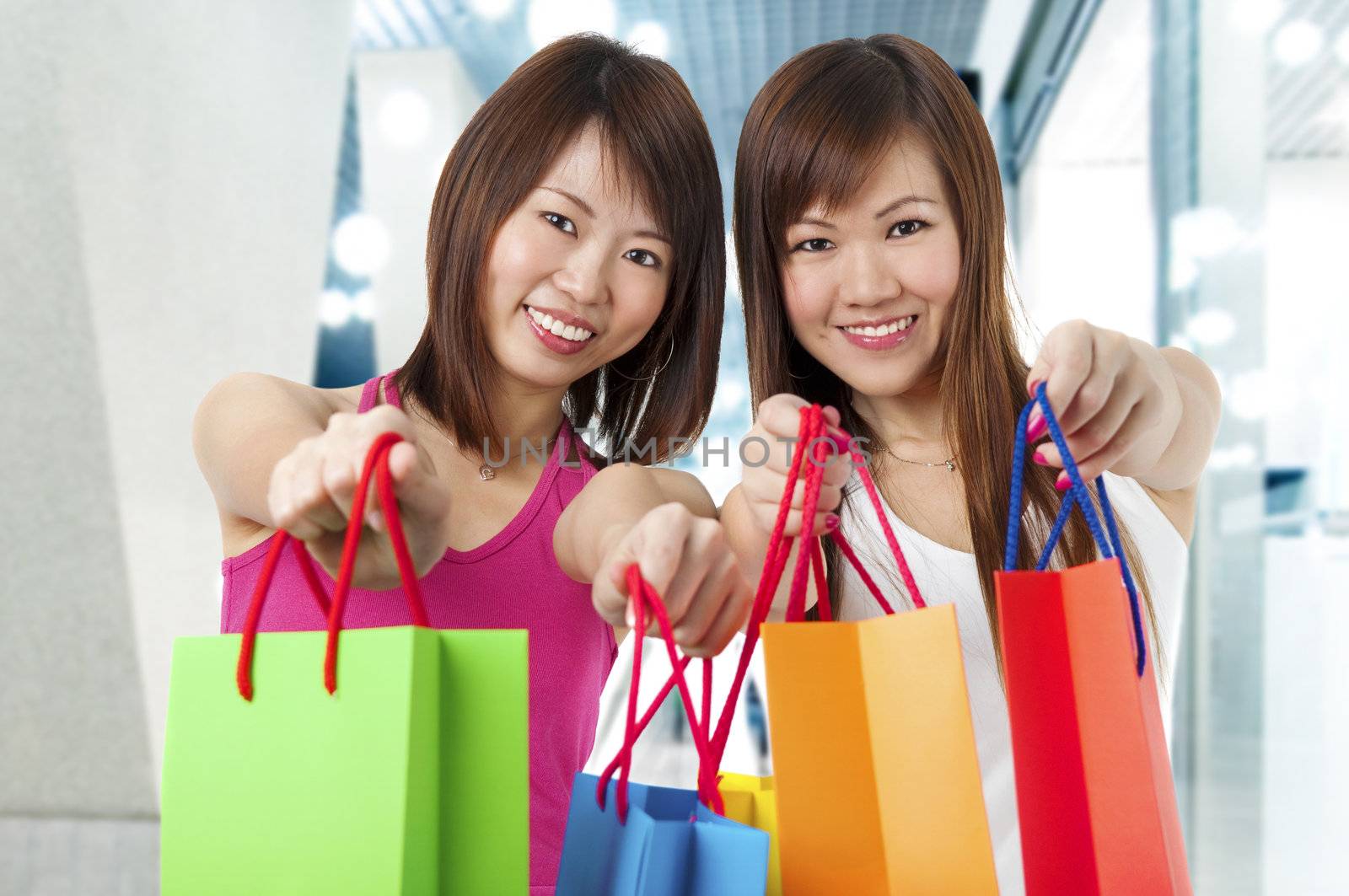 Happy Asian girls standing with shopping bags, shopping mall as background.