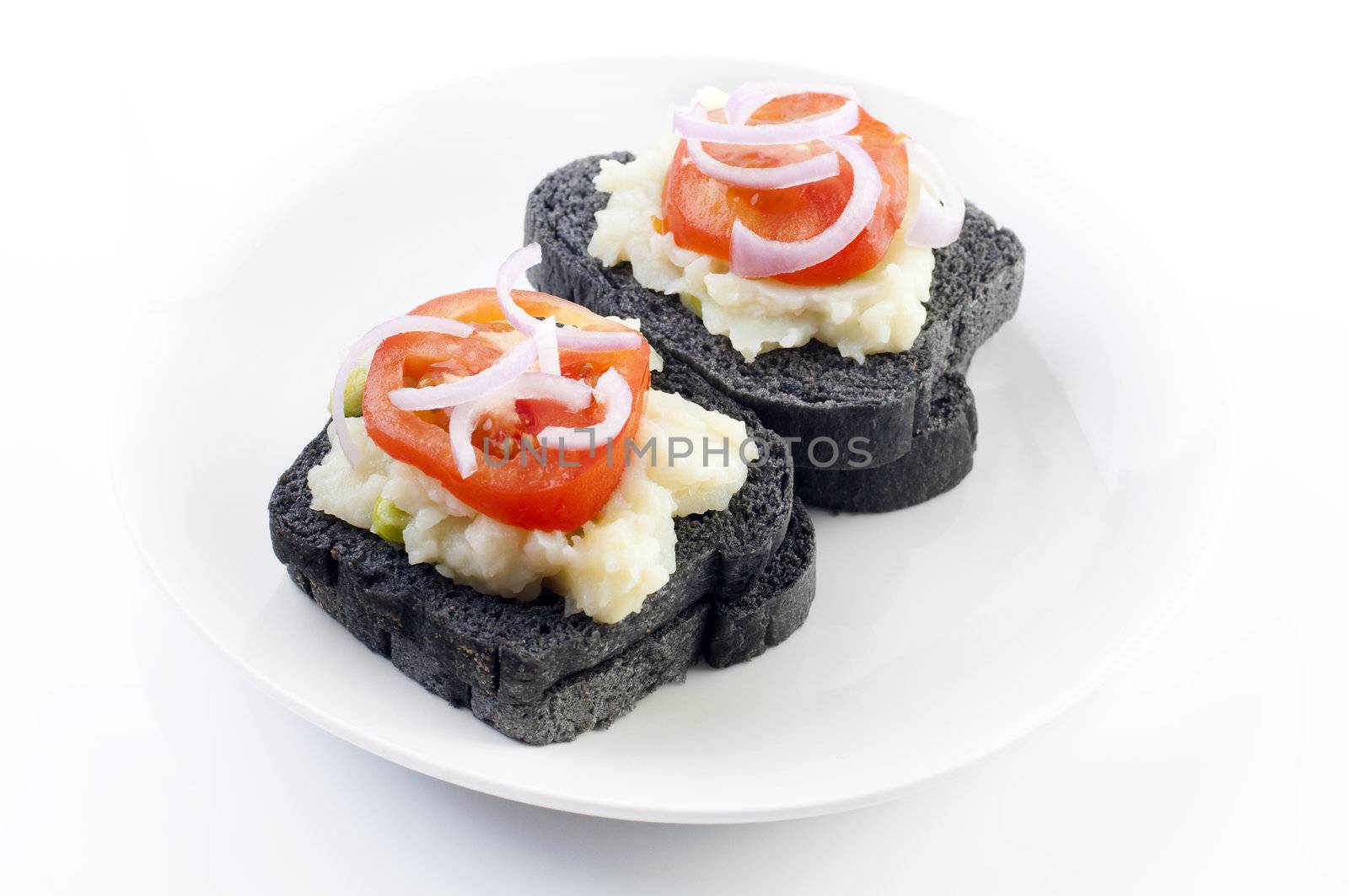 Black charcoal sandwich topped with mashed potato, tomato and onion.