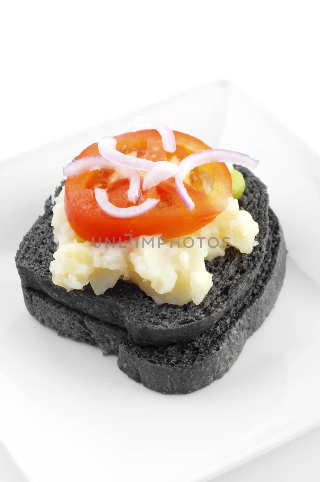 Black charcoal sandwich topped with mashed potato, tomato and onion.