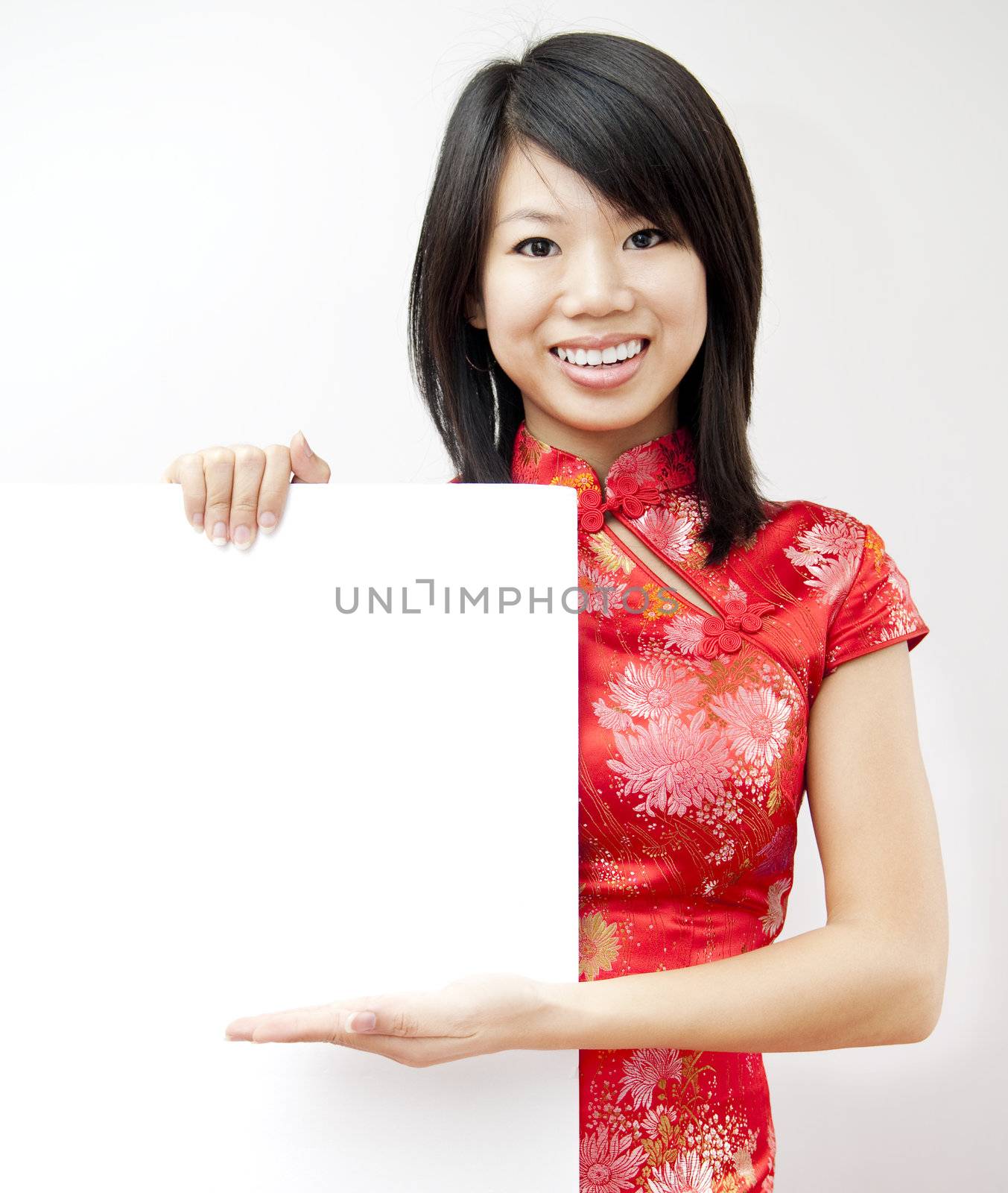 A smiling Oriental girl holding blank sign on grey background