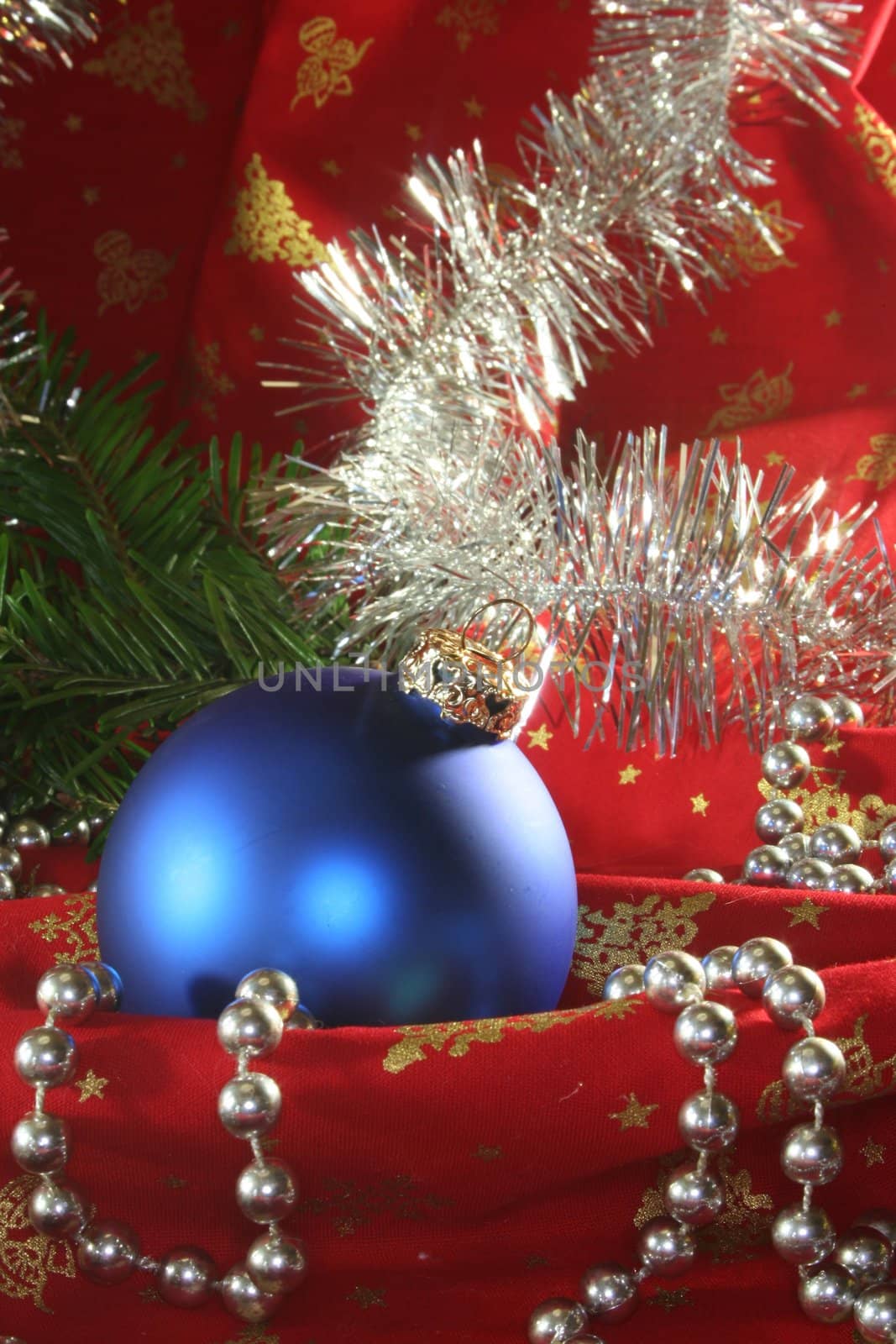 a blue Christmas ball and tinsel chain lie on red fabric