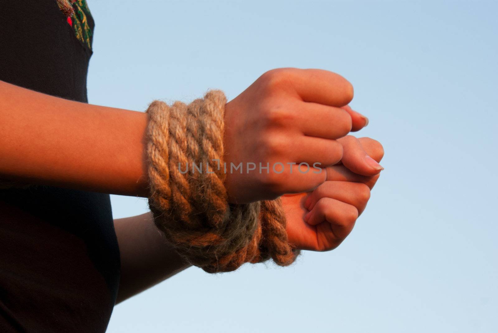 Hands tied up with rope against blue sky