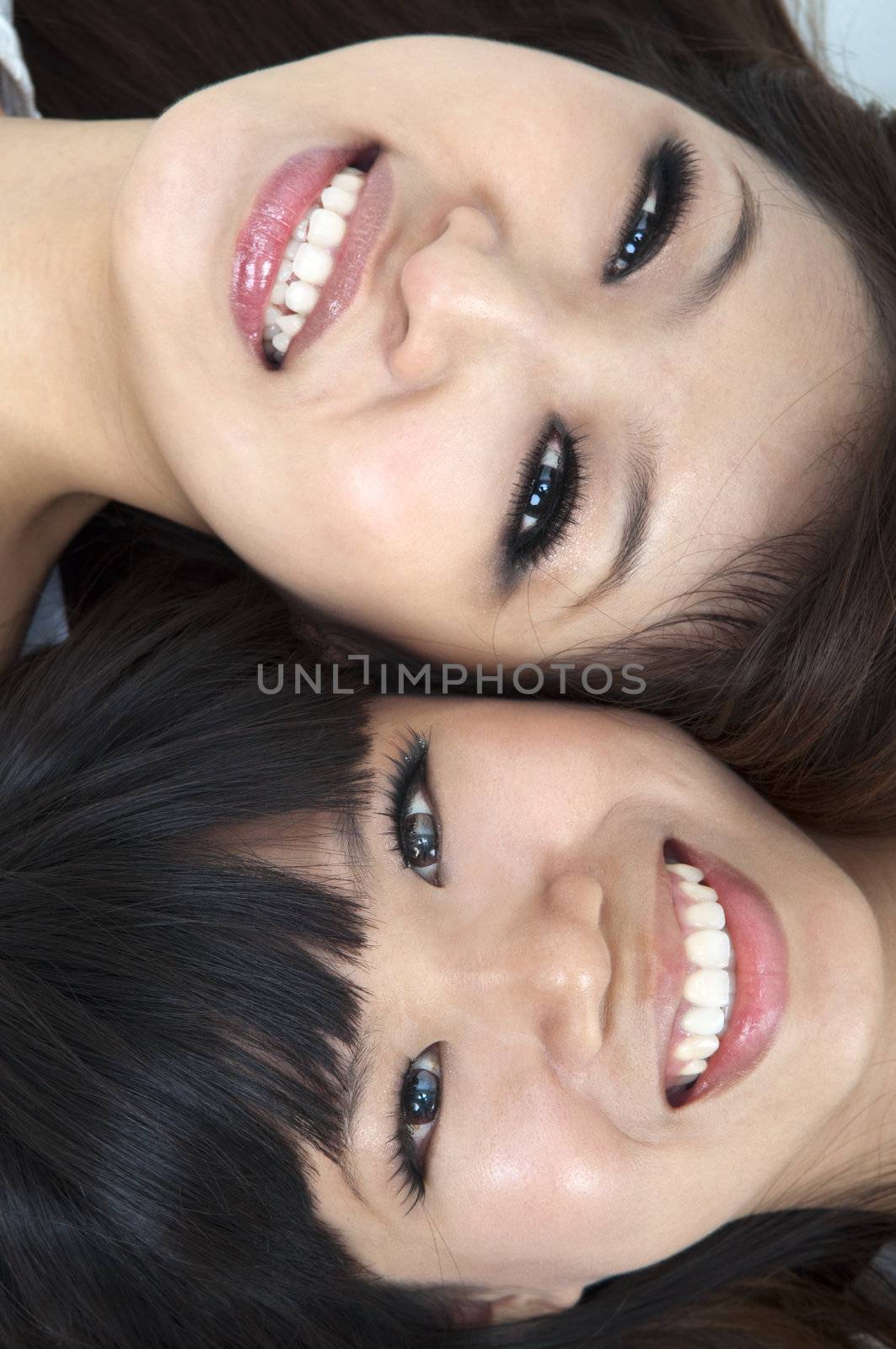 Closeup portrait of happy young girls lying on ground with their heads together 