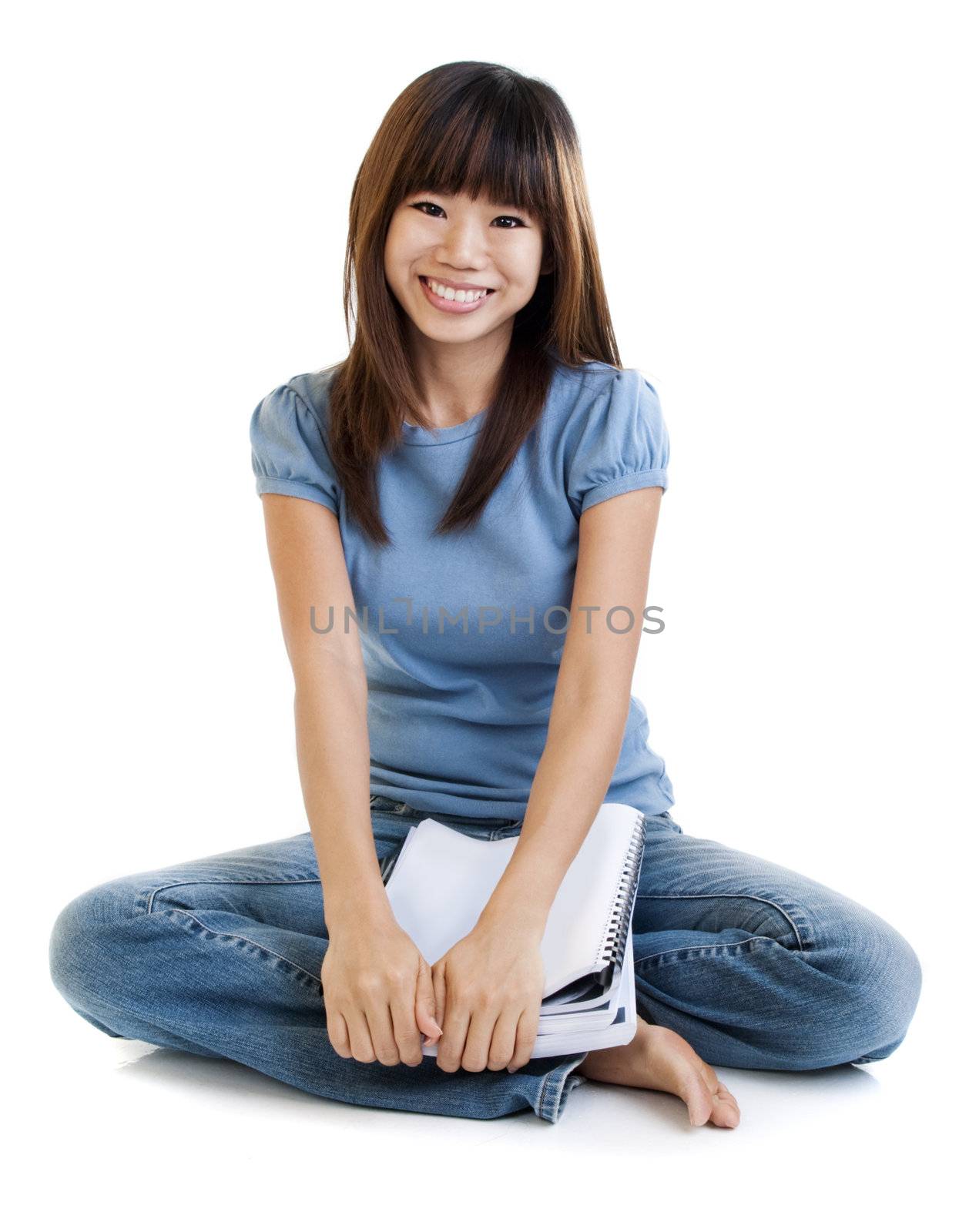 Asian student sitting on floor, with cheerful expression.