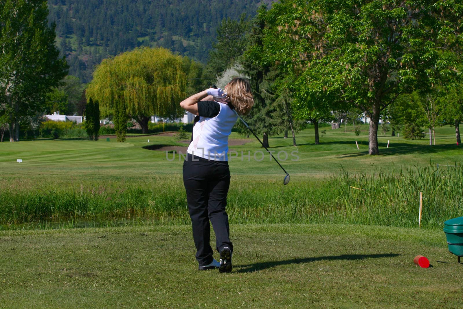 Blond female golfer following her shot from the tee-box down the fairway