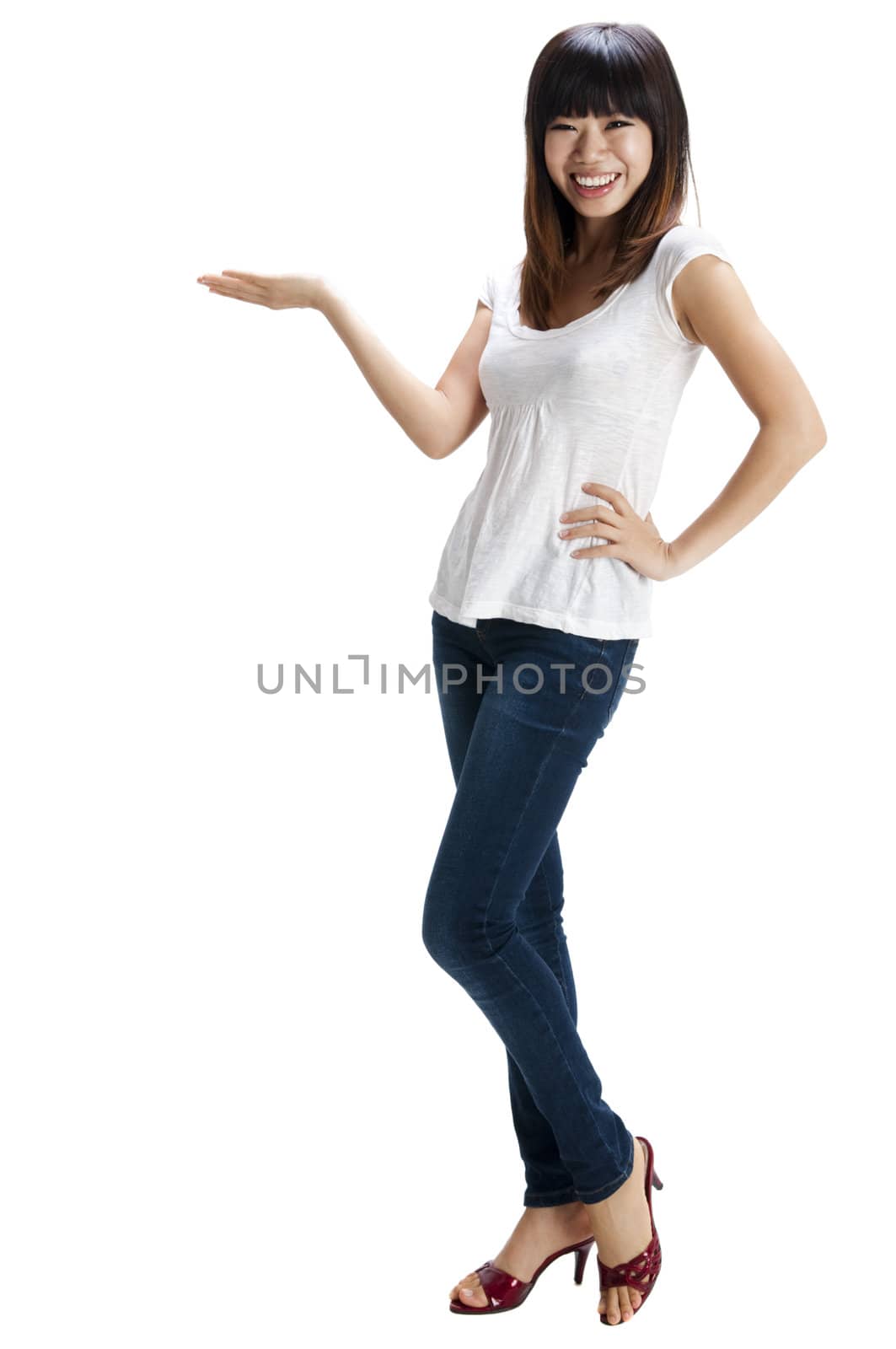 Full length of happy cheerful Asian young woman holding her hand out and showing copy space for your product.