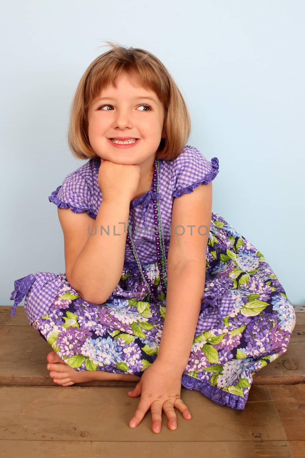 Cute little girl sitting on a wooden chest daydreaming