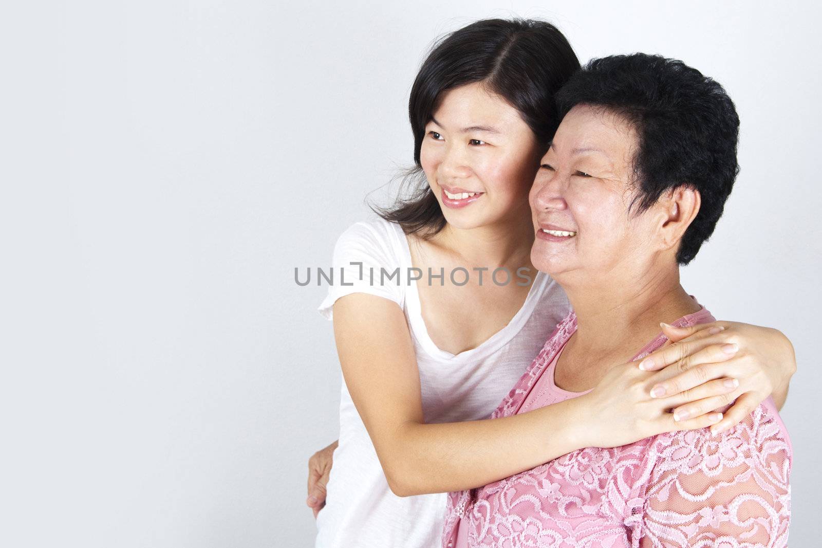 Senior Asian woman and young daughter looking away with smiling, on grey background.