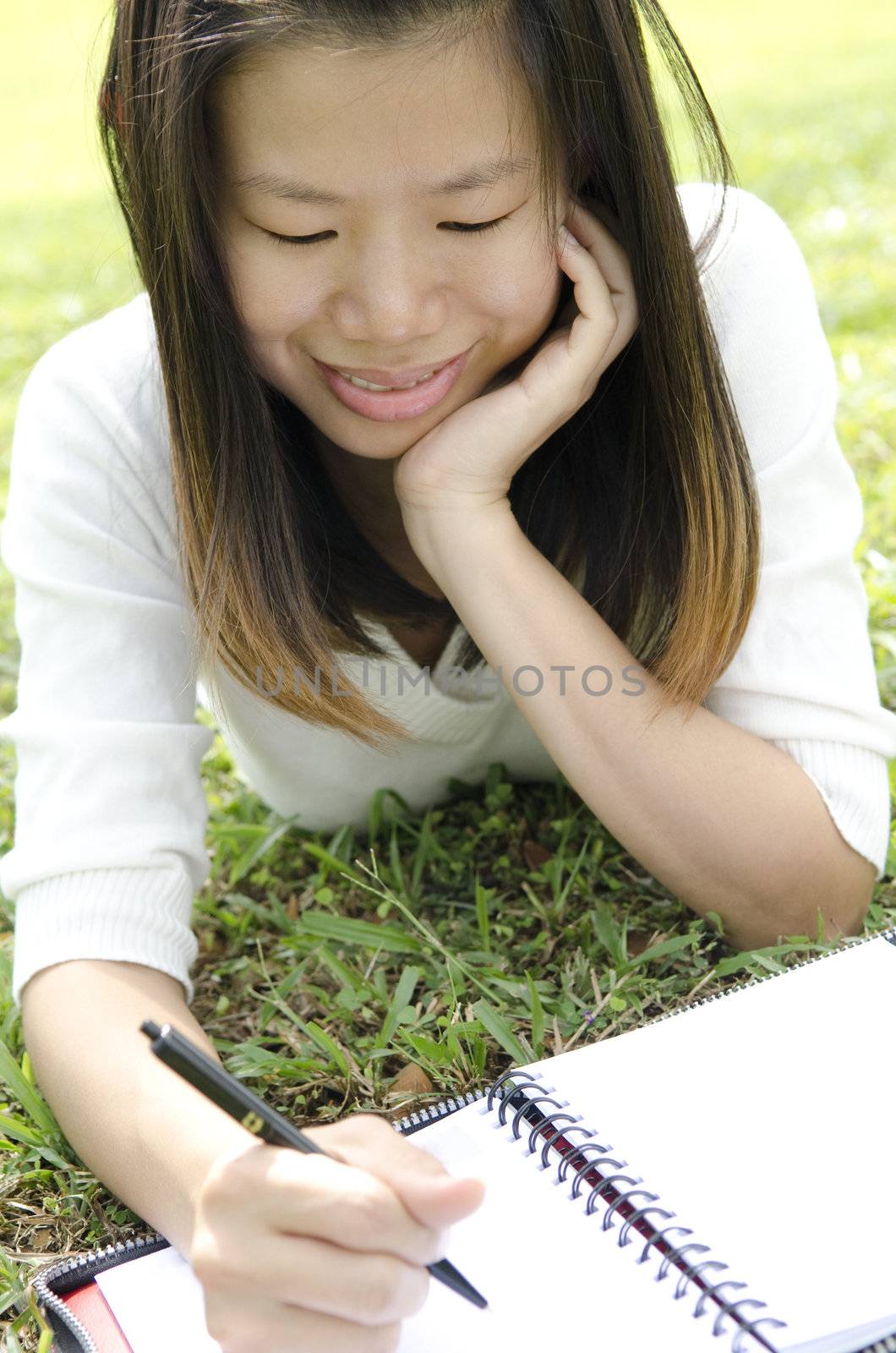 Asian student studying and writing at outdoors, lying on ground.