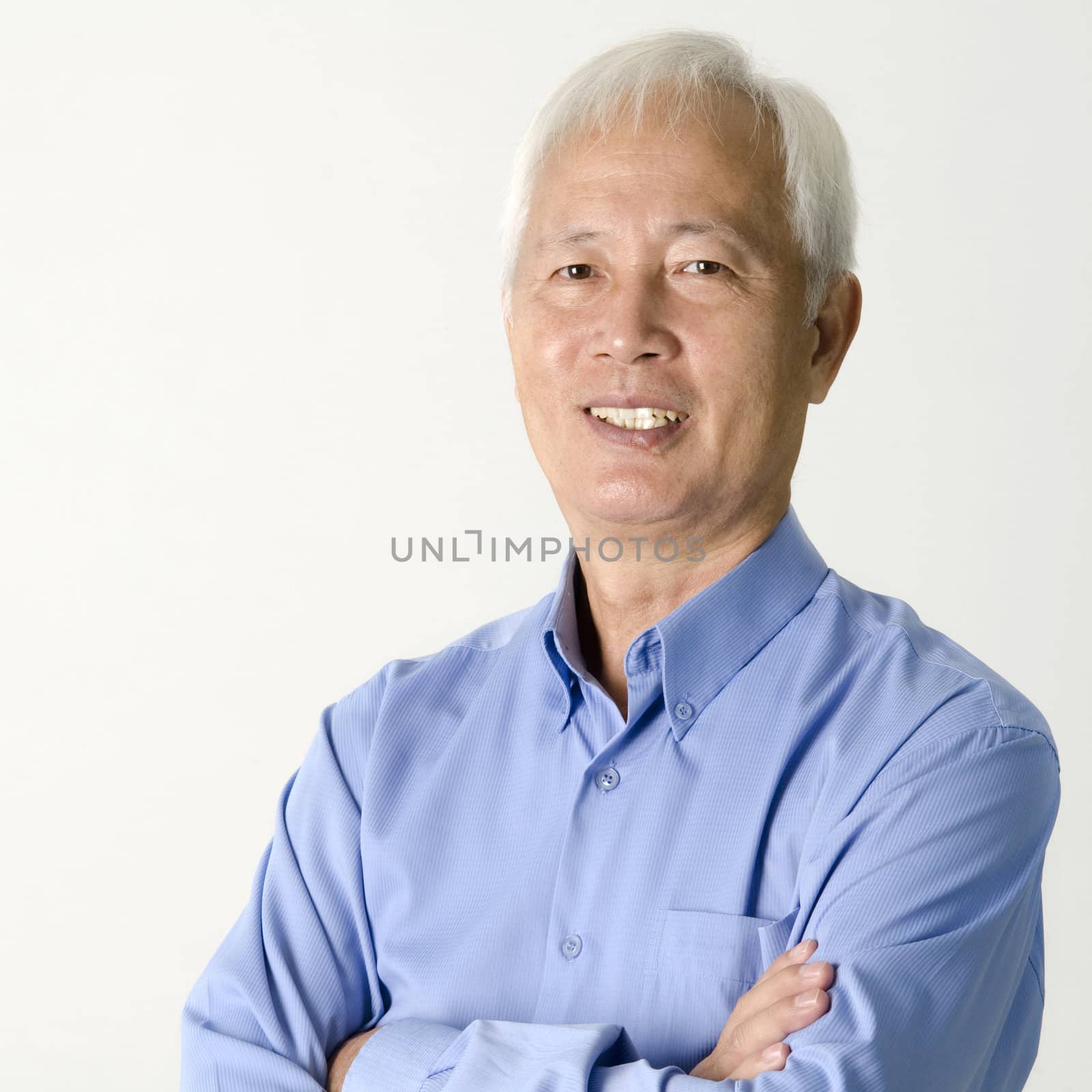 Crossed arms senior Asian businessman smiling on plain background