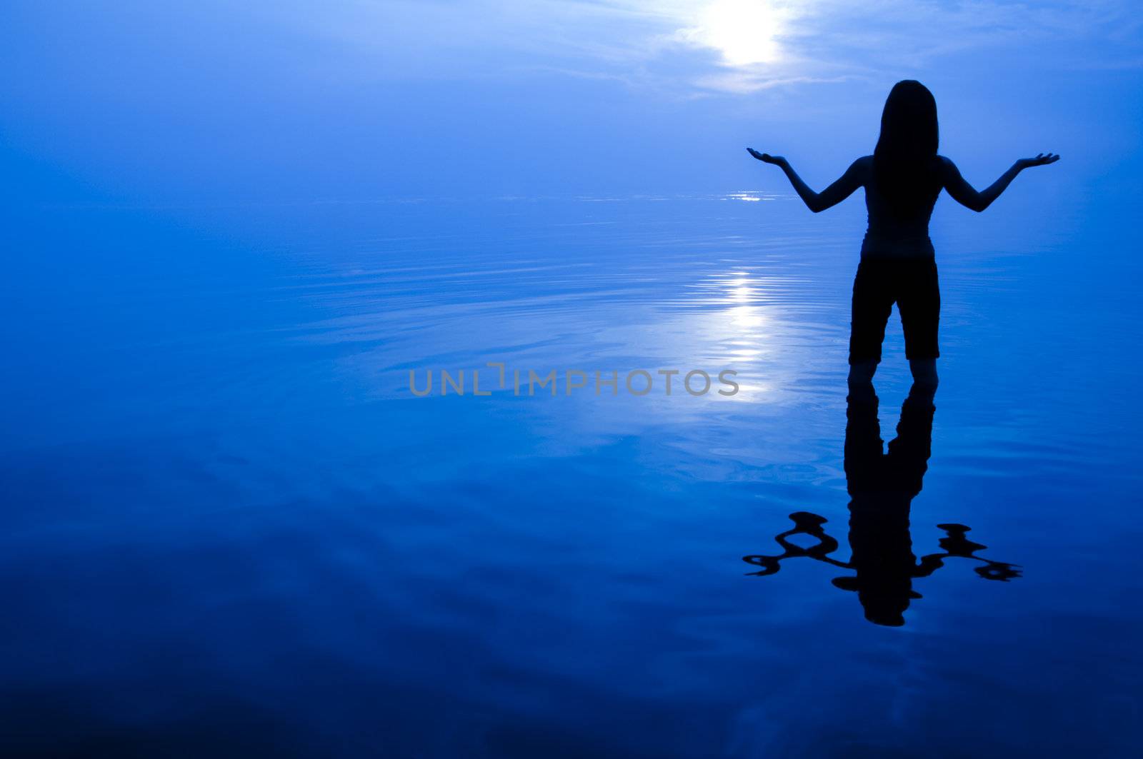 Abstract women silhouette in the sea looking at sun with arms open.