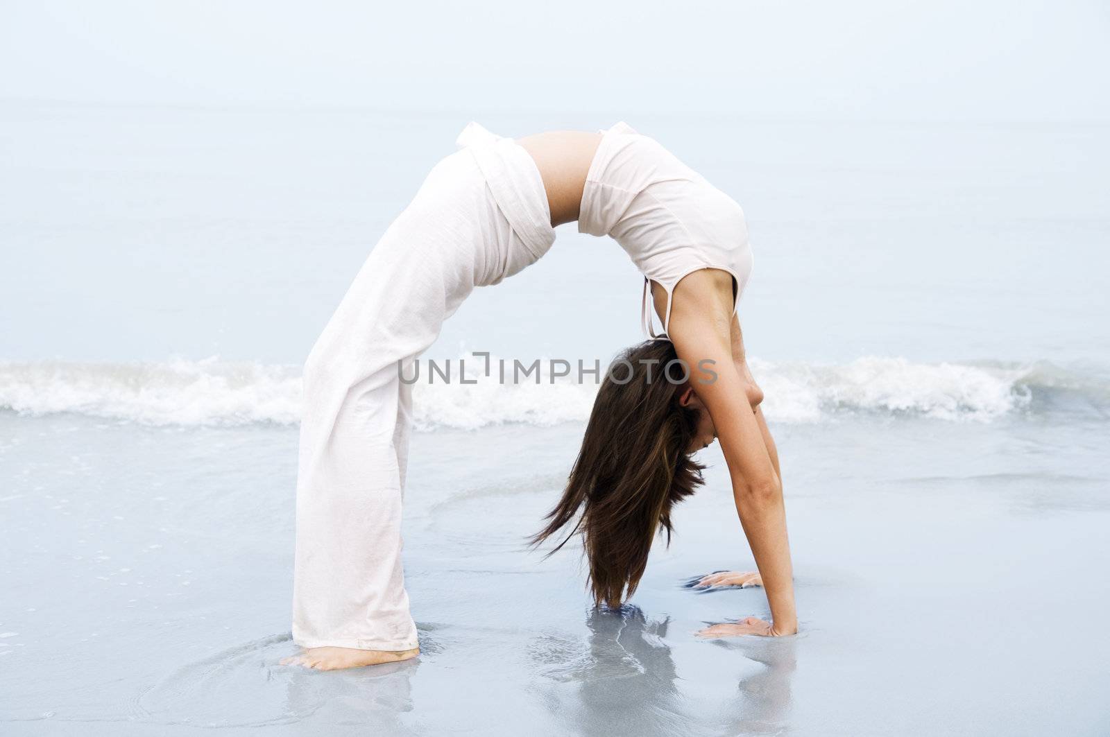 Woman practising Bridge Position Yoga on the beach.