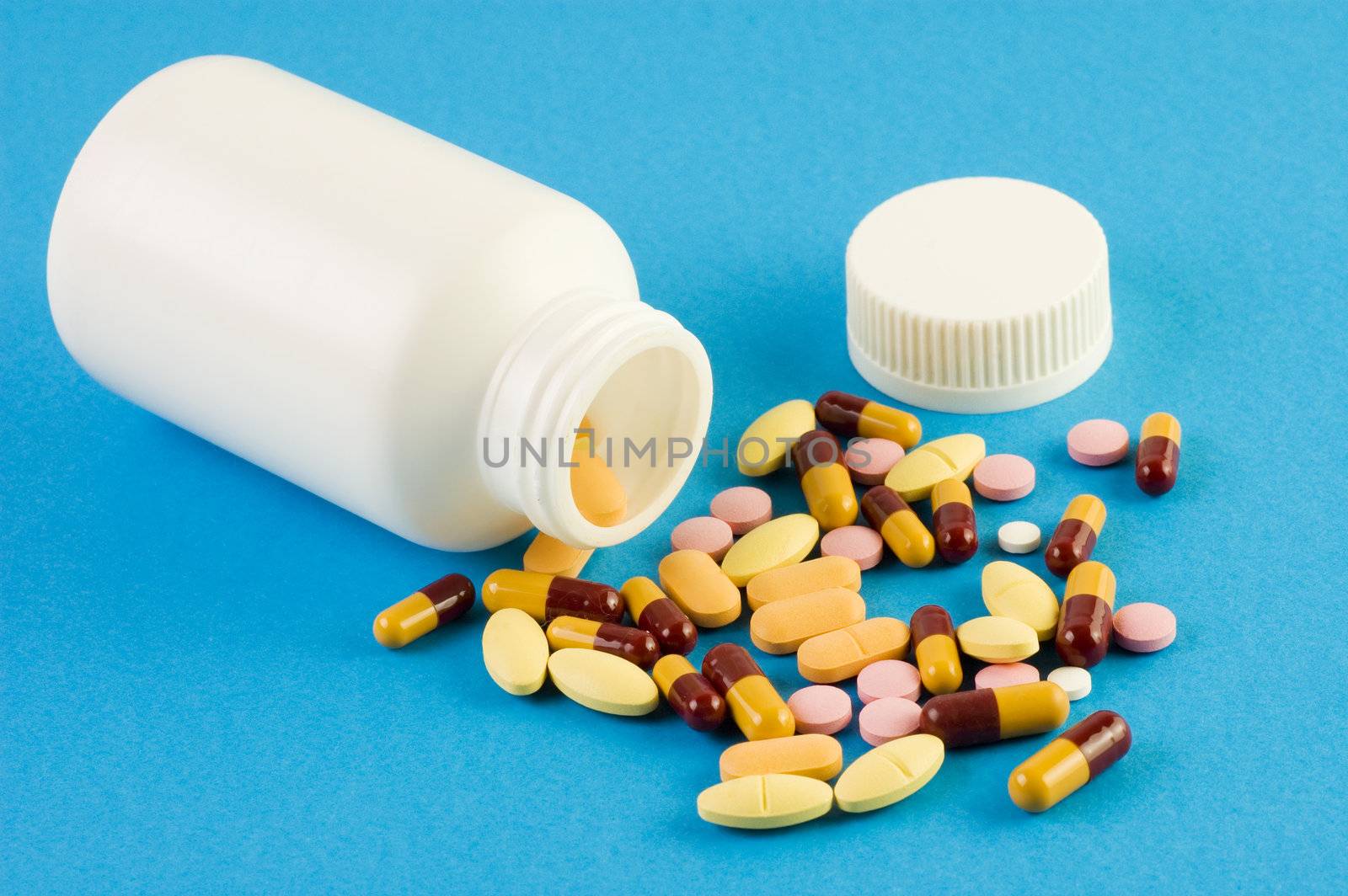 Pills spilled out of a bottle and scattered on blue background. 