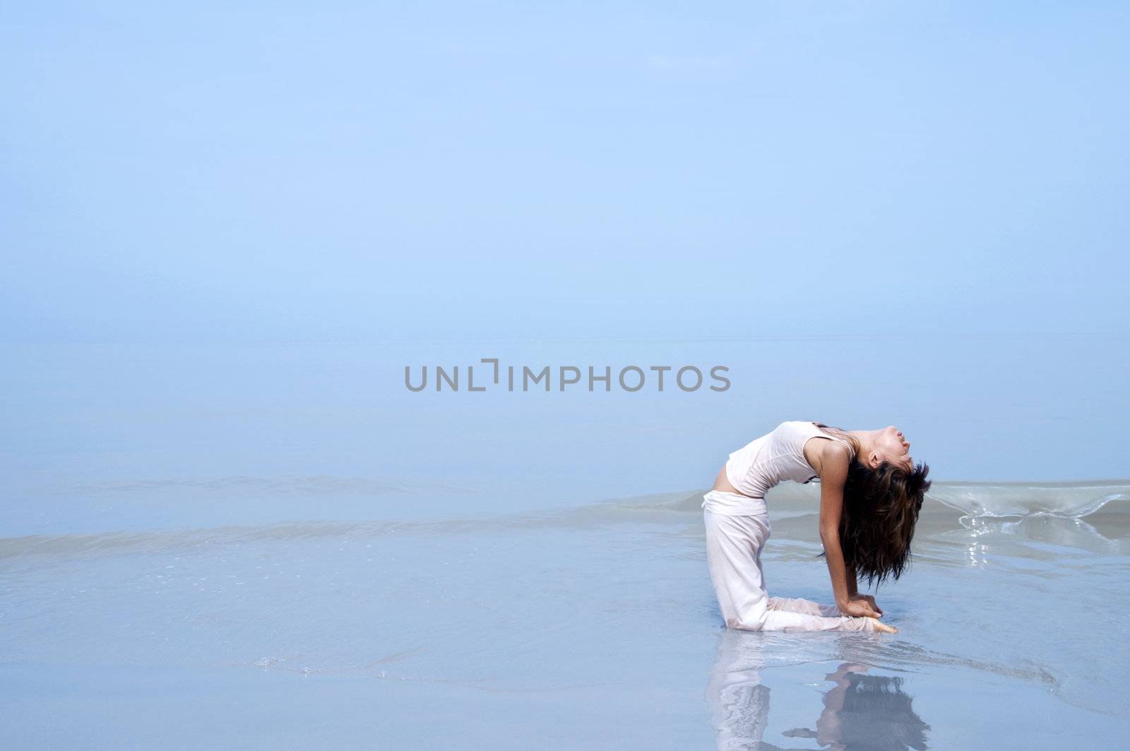 Woman practising Yoga(Camel Pose) on the beach.
