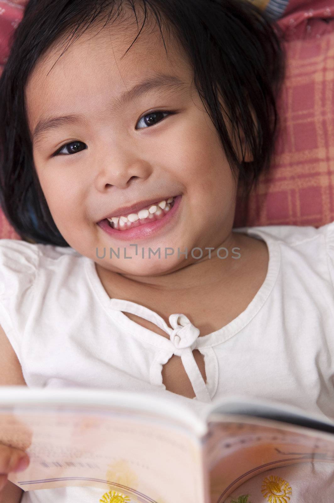 Little Asian girl lying on bed and reading 
