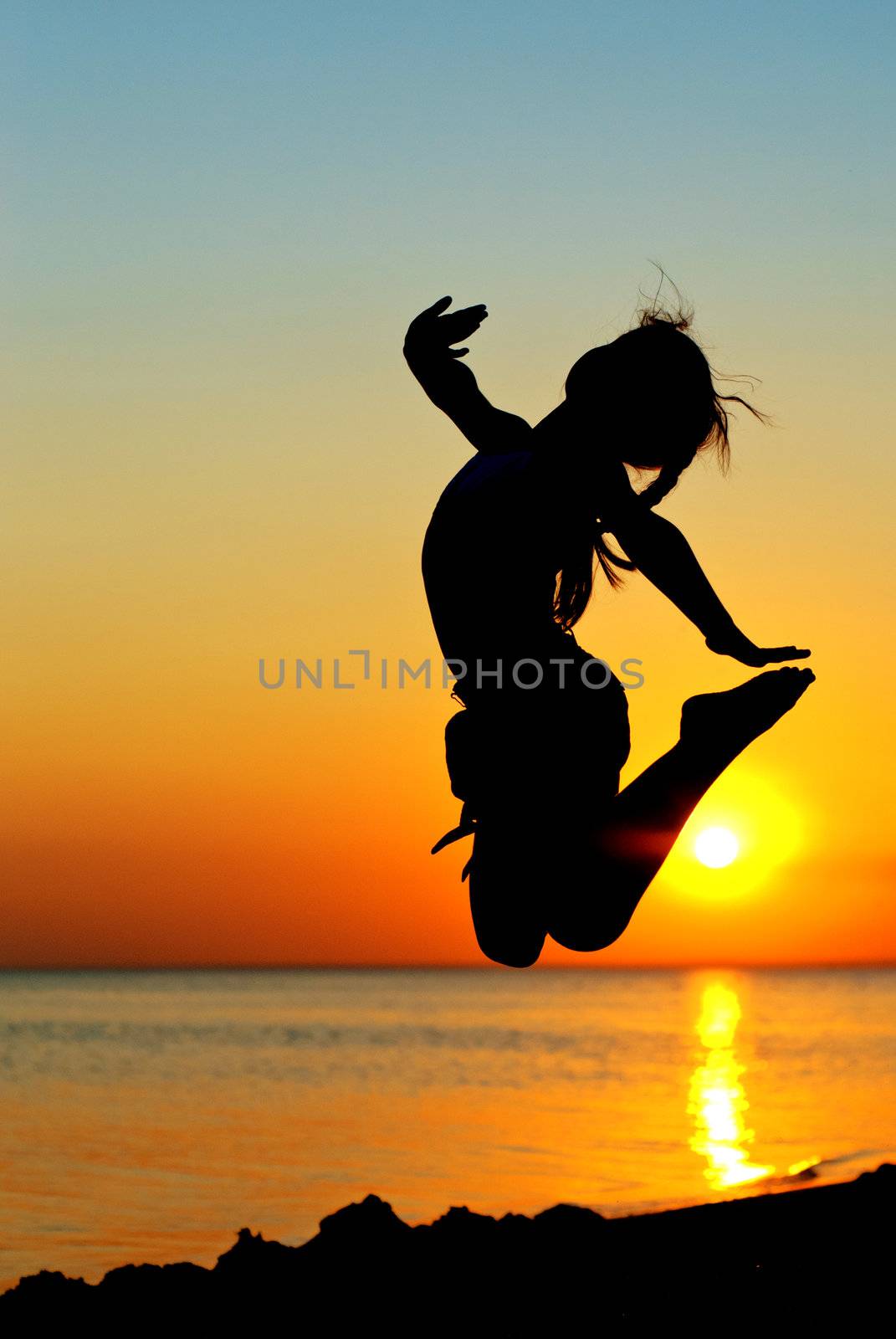 Jumping little girl on the beach at sunset