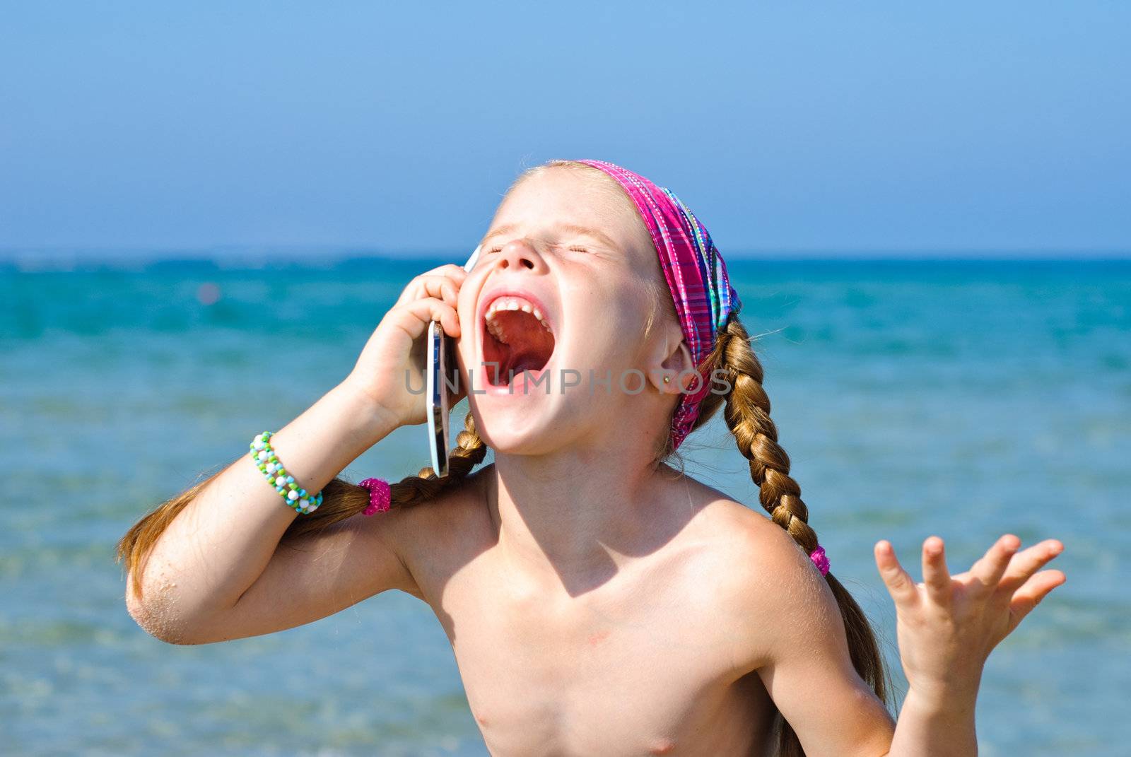 A little girl cries to mobile phone on the beach